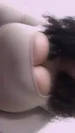 A close-up of a busty person with curly dark hair wearing a tight white shirt.