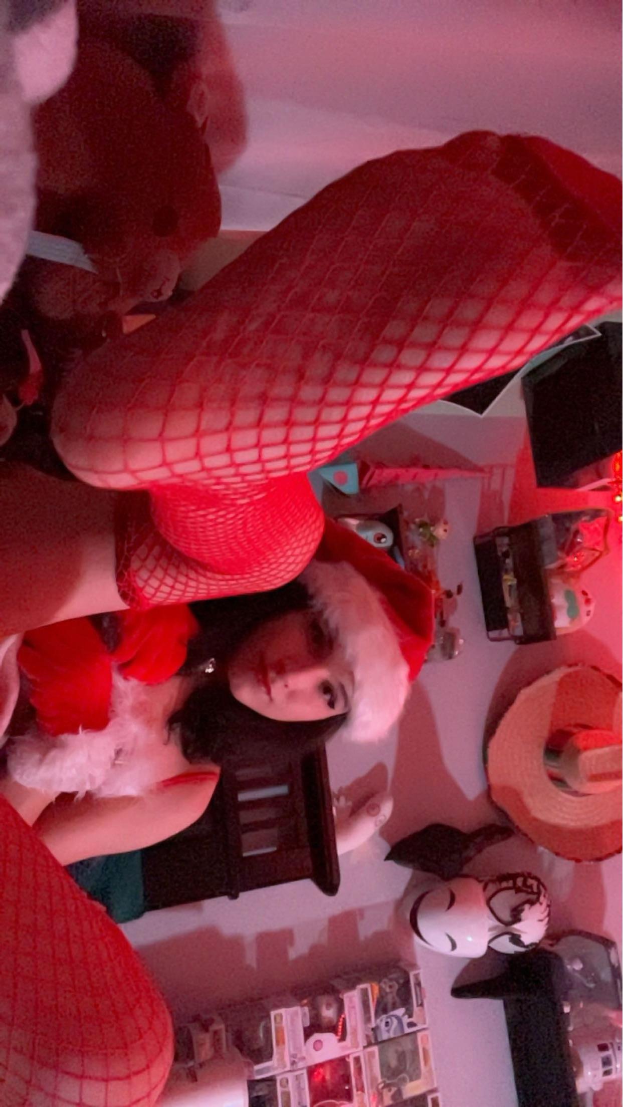 Curvy latina in a Santa hat, red lingerie, and fishnet stockings posing for selfies in a bedroom