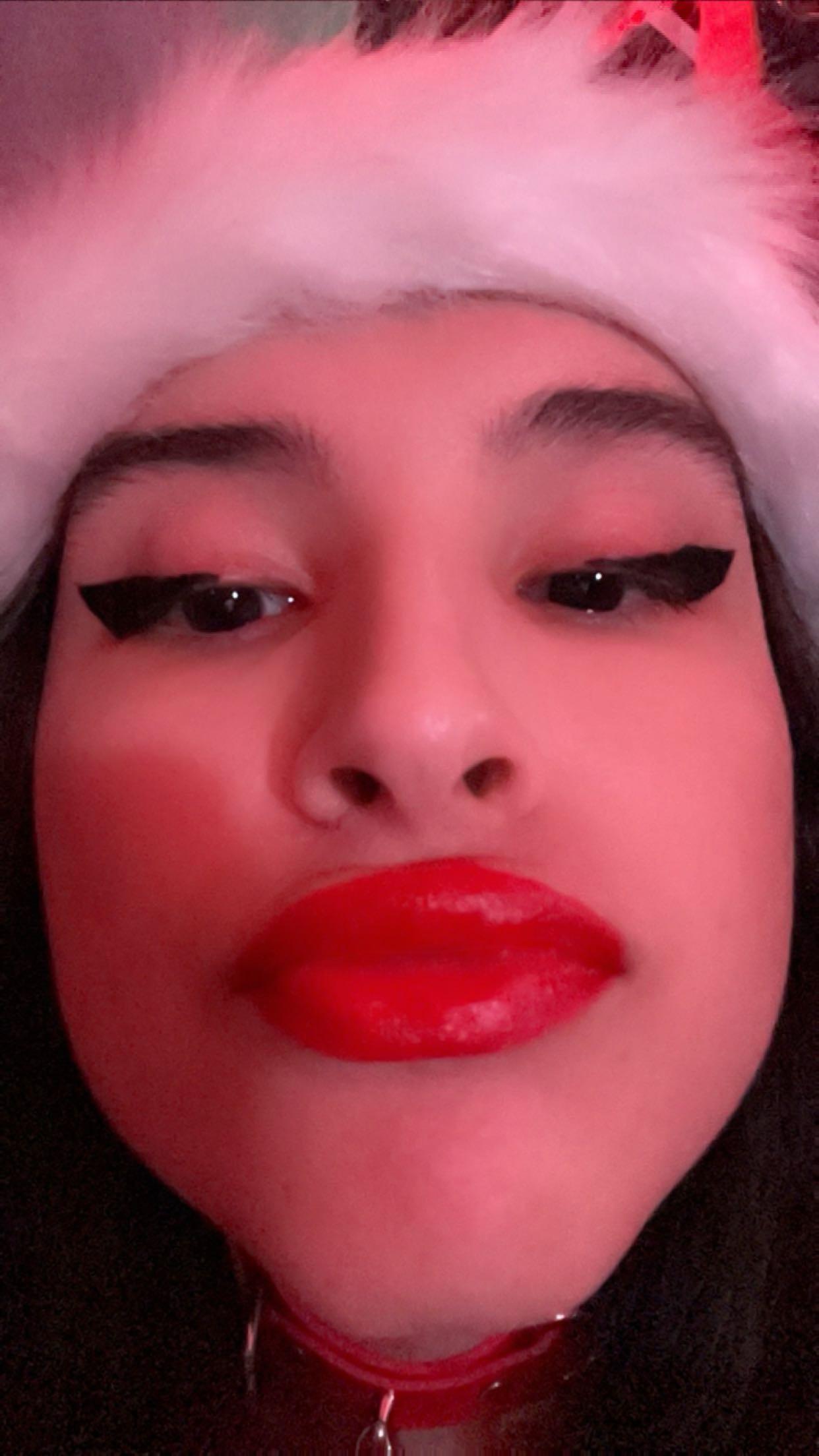 Curvy latina in a Santa hat, red lingerie, and fishnet stockings posing for selfies in a bedroom