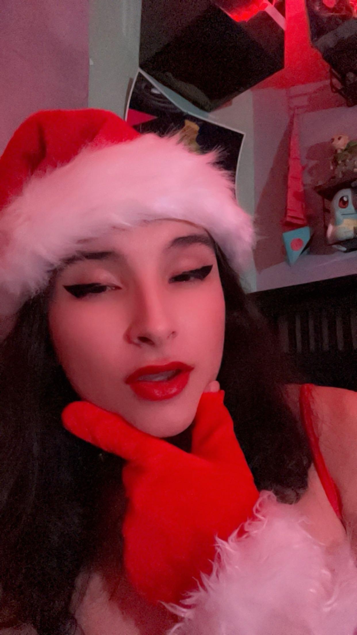 Curvy latina in a Santa hat, red lingerie, and fishnet stockings posing for selfies in a bedroom