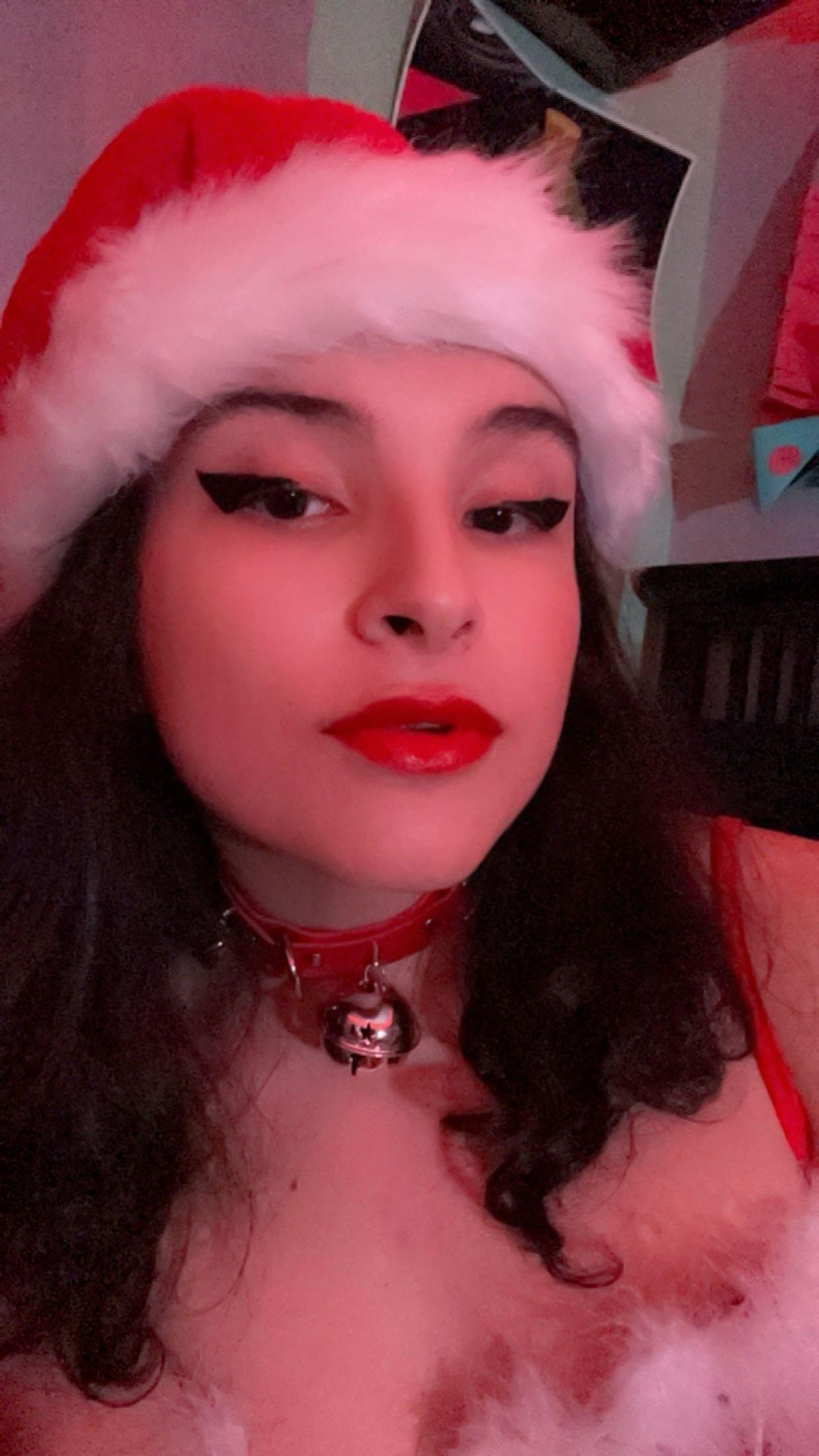 Curvy latina in a Santa hat, red lingerie, and fishnet stockings posing for selfies in a bedroom