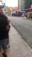 A man in a yellow shirt drives a mobility scooter with a woman in a floral dress lying on the front before she falls off.