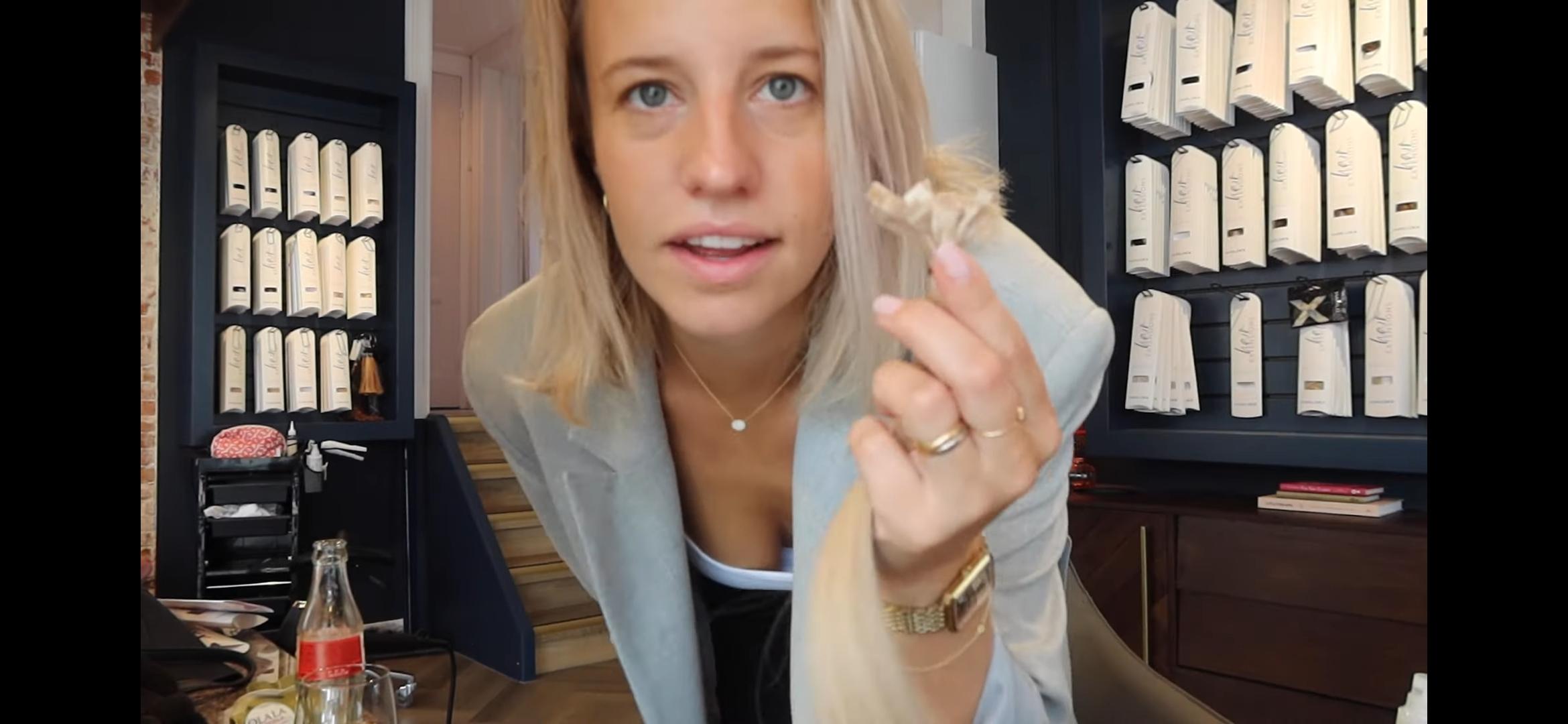 Dee, a slim blonde woman in a light blazer and white blouse, showing off her long hair extensions in a selfie.