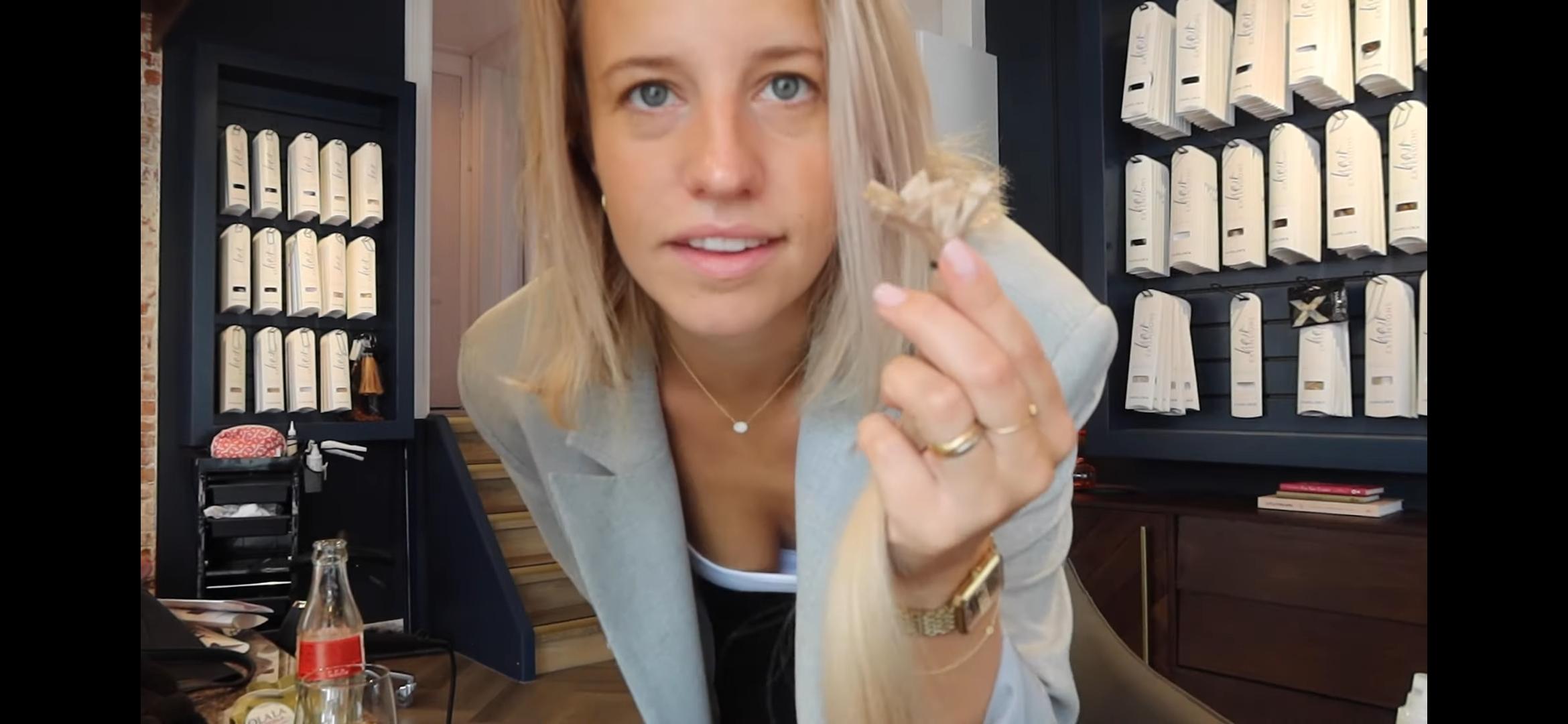 Dee, a slim blonde woman in a light blazer and white blouse, showing off her long hair extensions in a selfie.