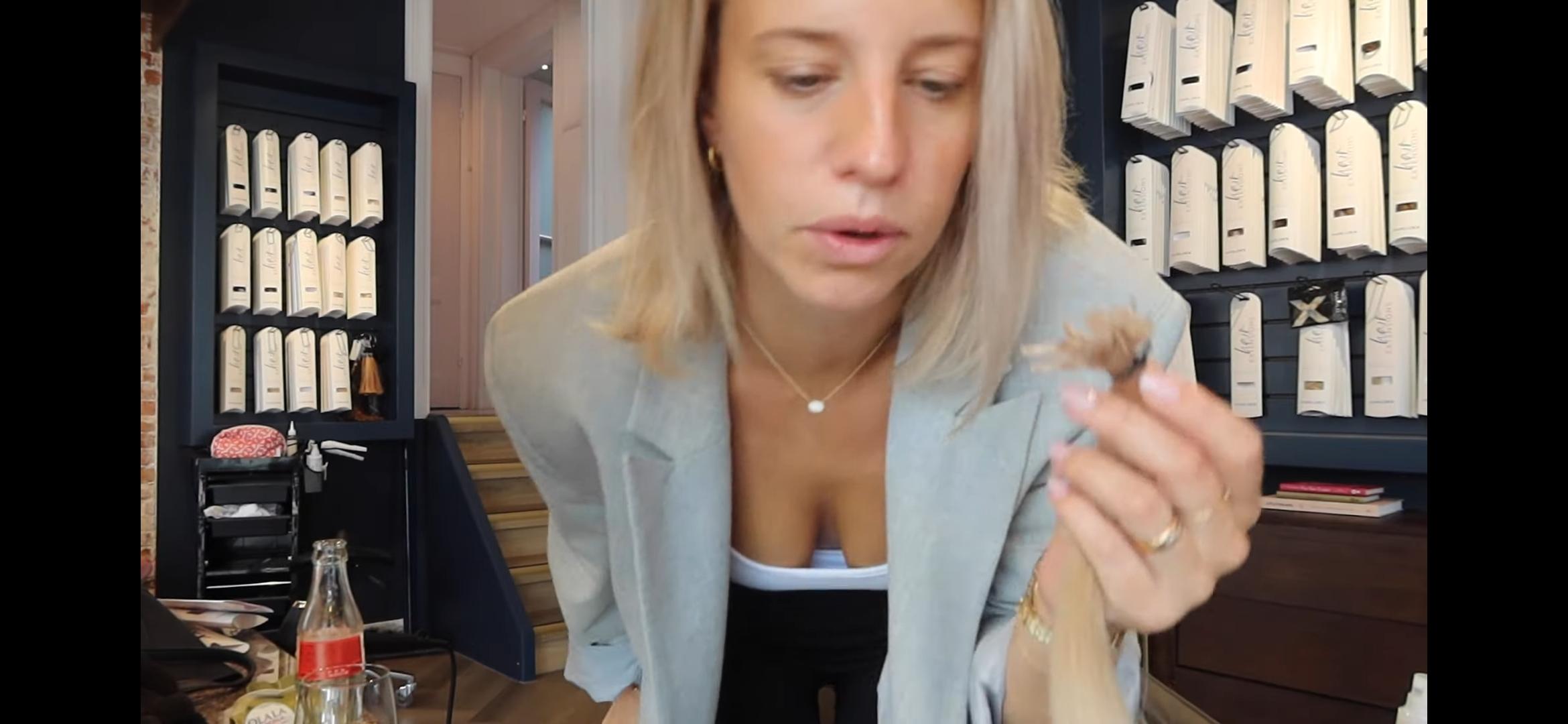Dee, a slim blonde woman in a light blazer and white blouse, showing off her long hair extensions in a selfie.