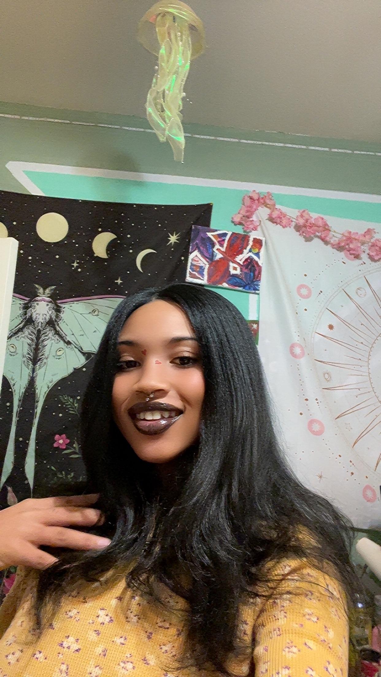 Mixed black girl with long black wavy hair in a yellow crop top and brown pants showing Calvin Klein underwear