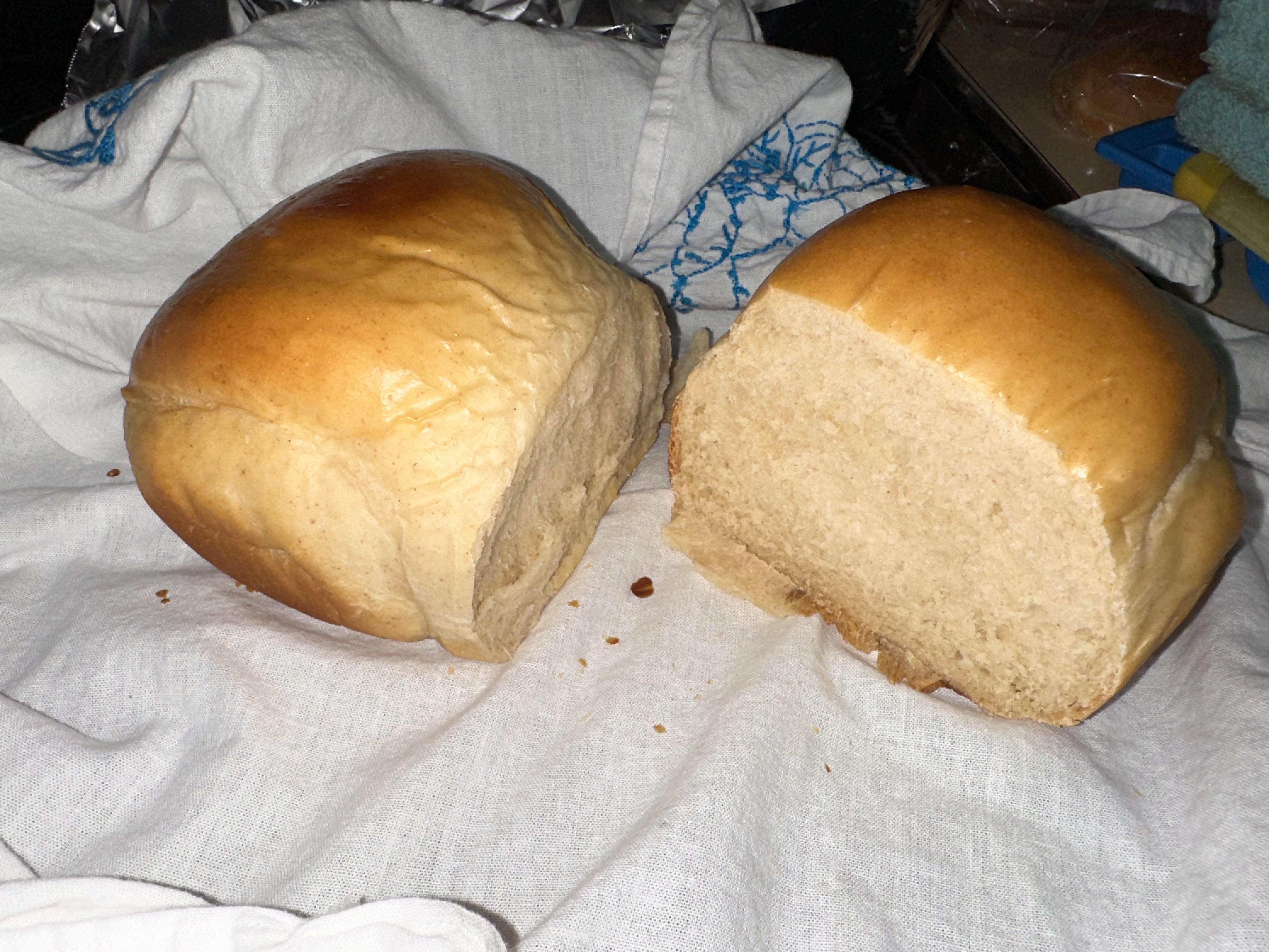 Two golden-brown homemade bread loaves resting on a white cloth.