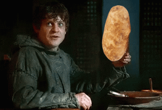 A man with curly brown hair in a grey tunic looking surprised while holding a large piece of bread
