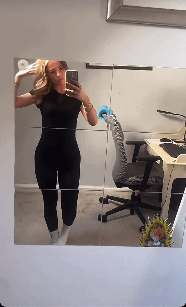 Curvy blonde woman in a black bodysuit and white socks taking a mirror selfie