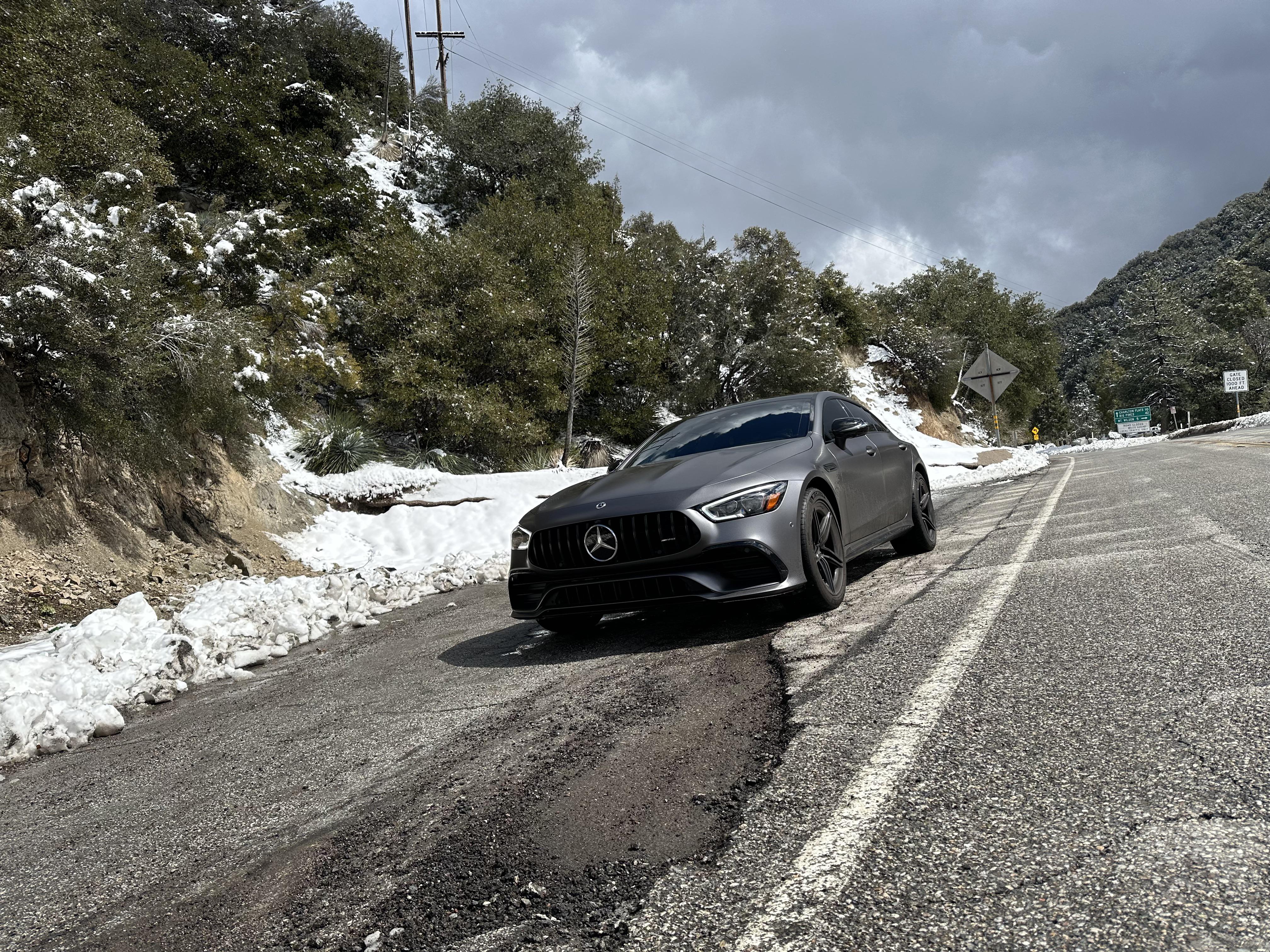 Grey BMW F90 M5 parked on a paved driveway with hedges and a hillside background