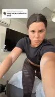 Desi Johnson in a black crop top and brown patterned spandex yoga pants stretching her back in a bedroom
