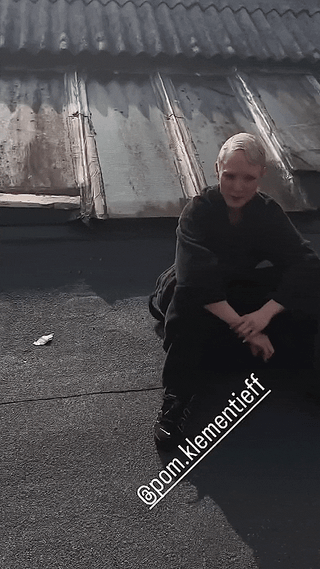 Pom Klementieff with short blonde hair in black clothing sitting on a rooftop making funny faces