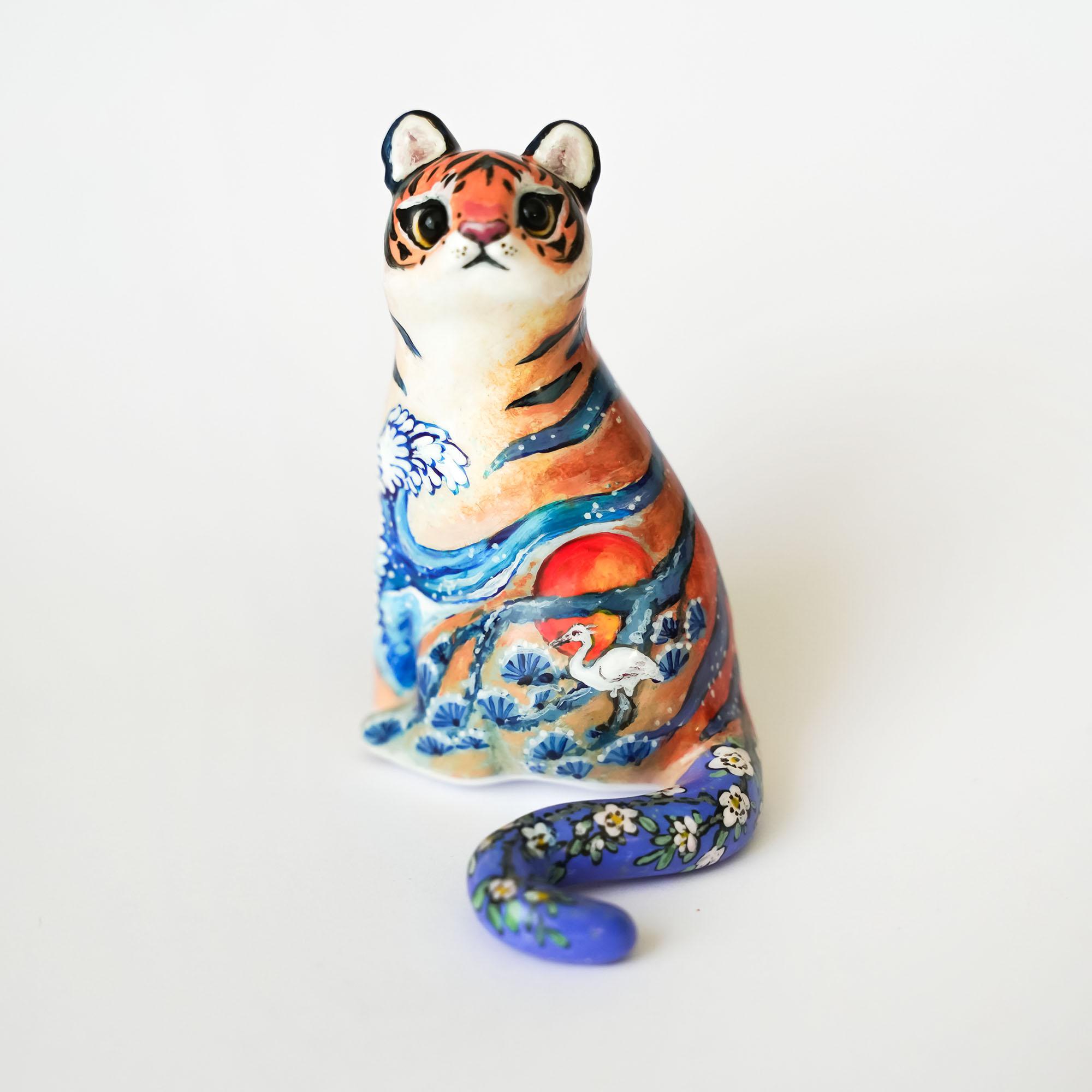Japanese tiger ceramic figurine with a colorful landscape painting of a sun, crane, and blue waves.
