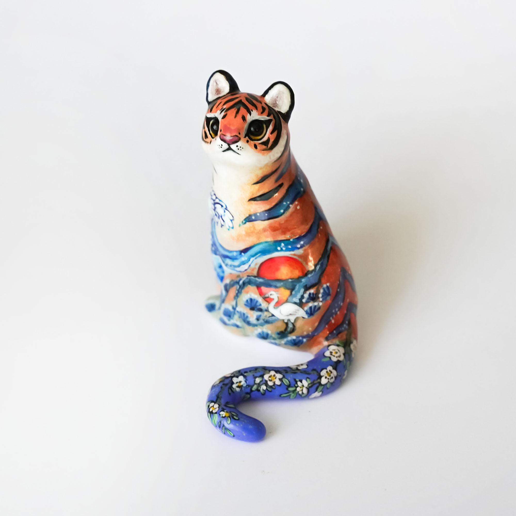 Japanese tiger ceramic figurine with a colorful landscape painting of a sun, crane, and blue waves.