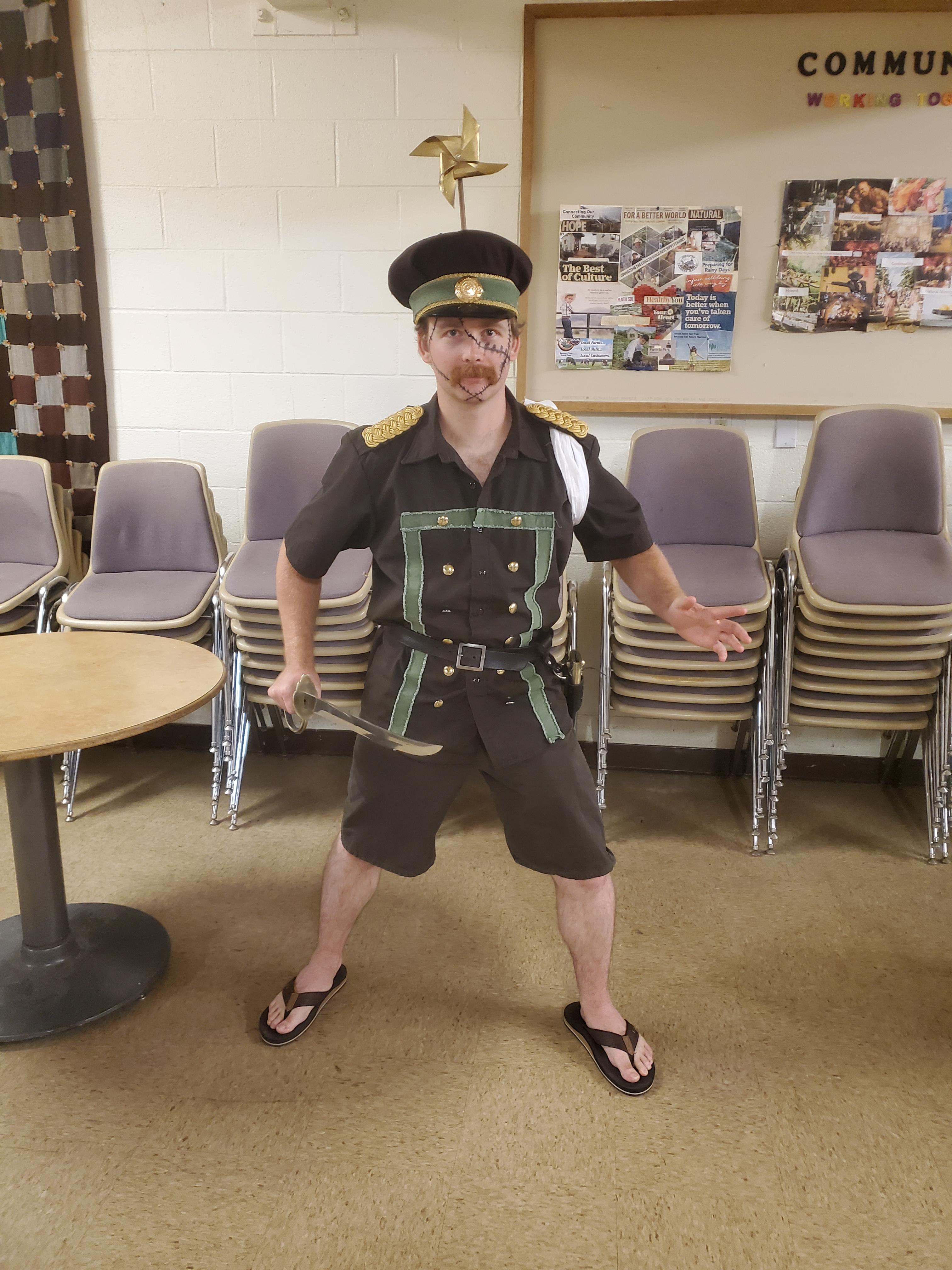 Genzo cosplay from One Piece featuring a man in a black captain's costume with short shorts and a gold pin hat