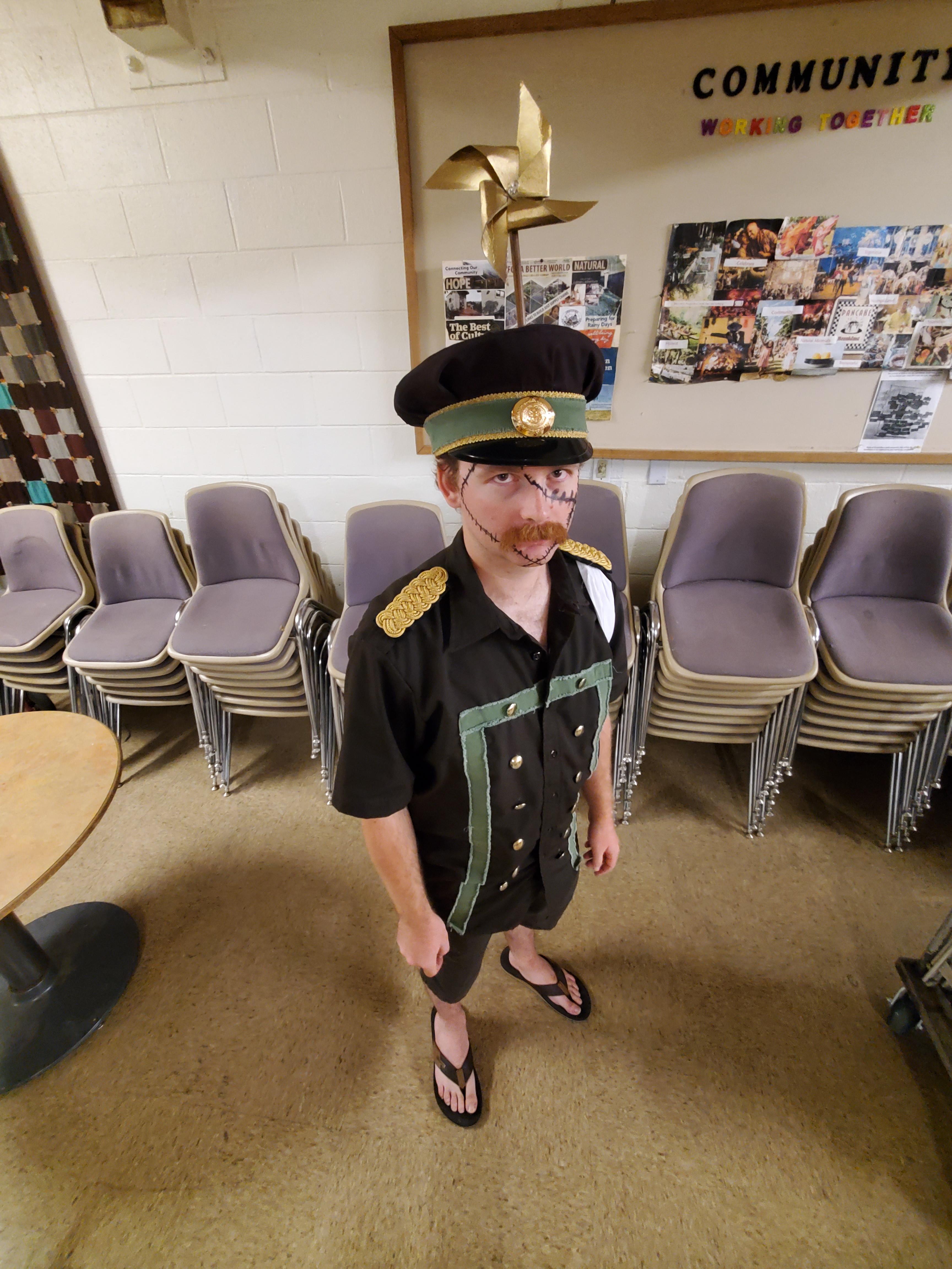 Genzo cosplay from One Piece featuring a man in a black captain's costume with short shorts and a gold pin hat