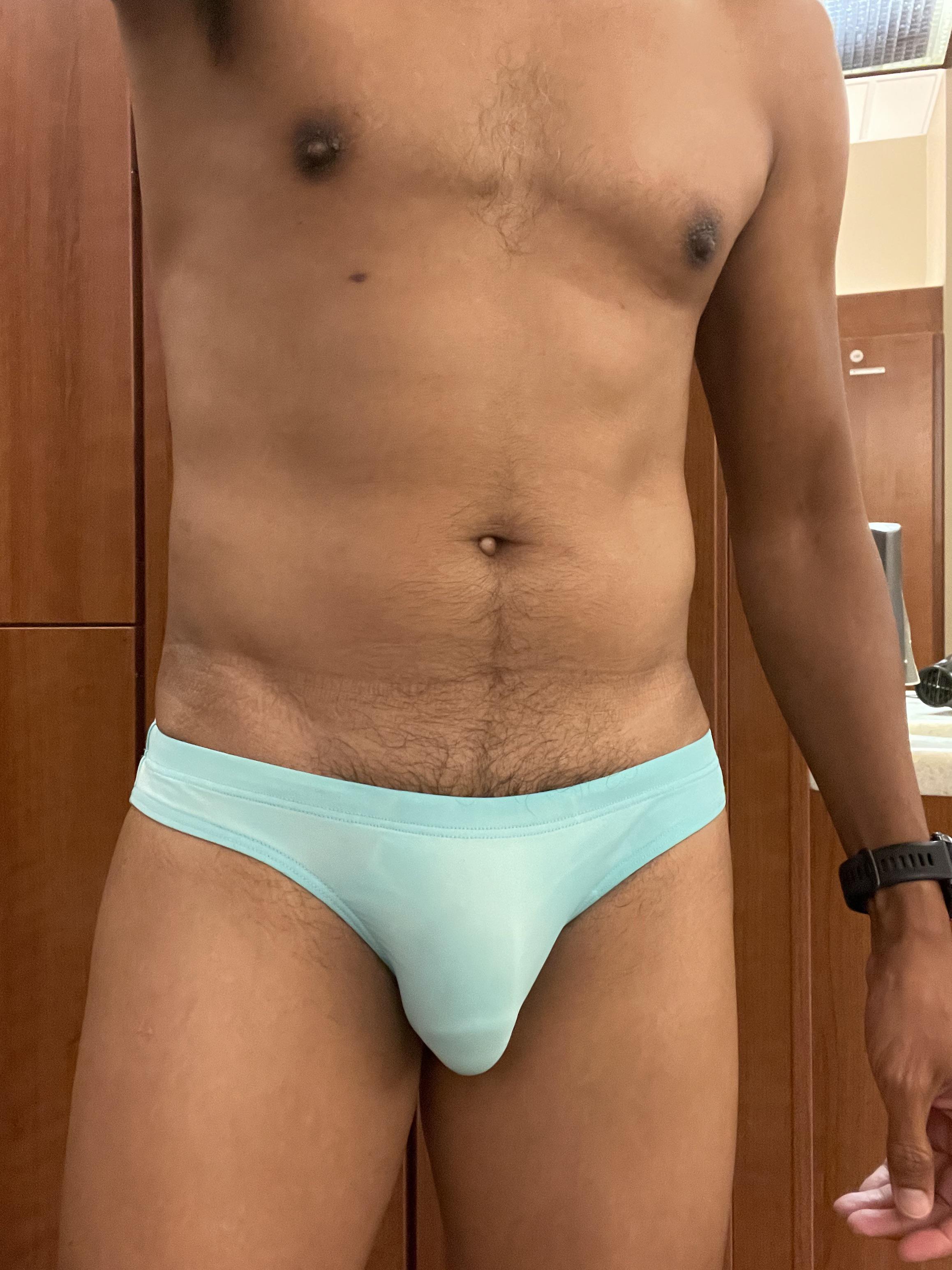 Muscular mixed man in light blue speedos posing in a locker room and swimming pool.