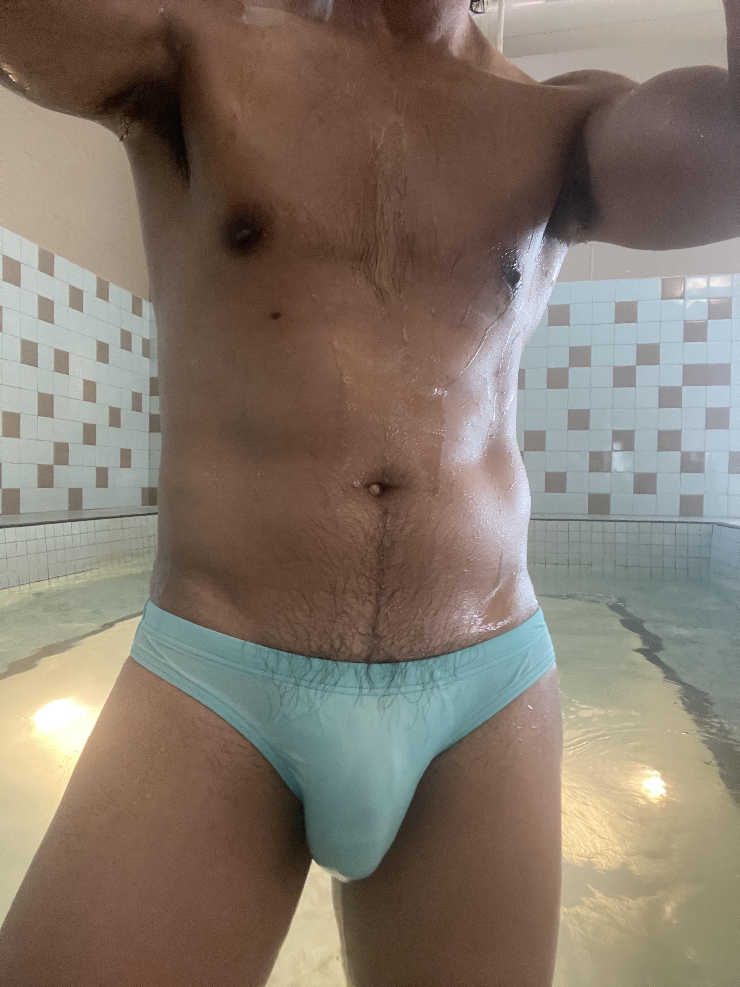 Muscular mixed man in light blue speedos posing in a locker room and swimming pool.