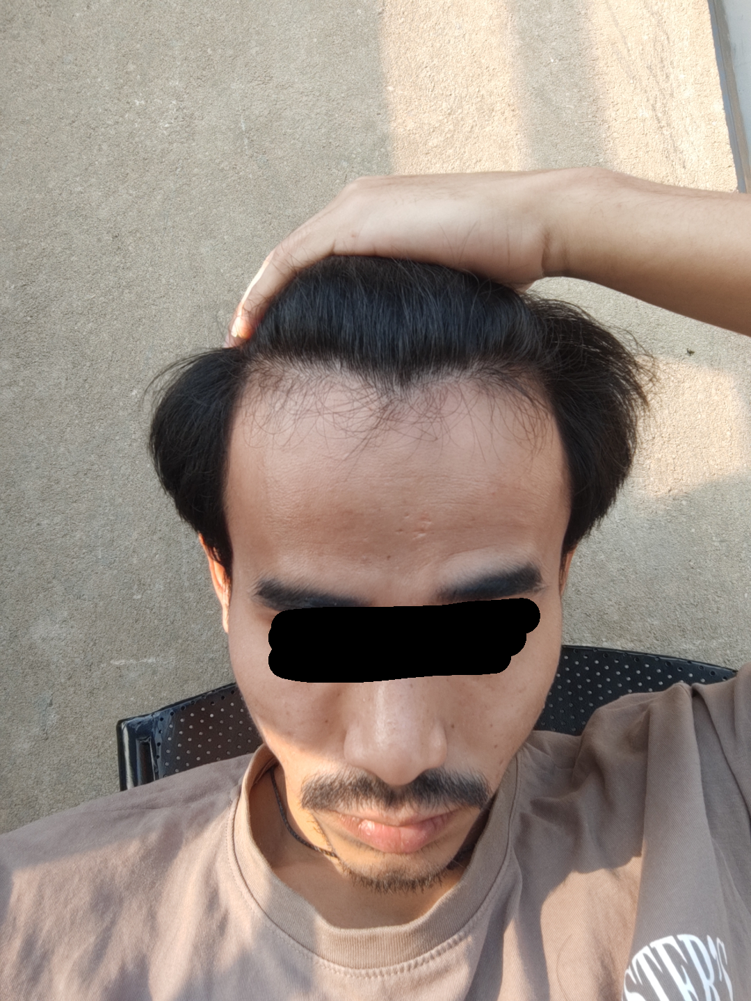 Man with black hair and a mustache in a brown t-shirt showing his hairline for male grooming suggestions