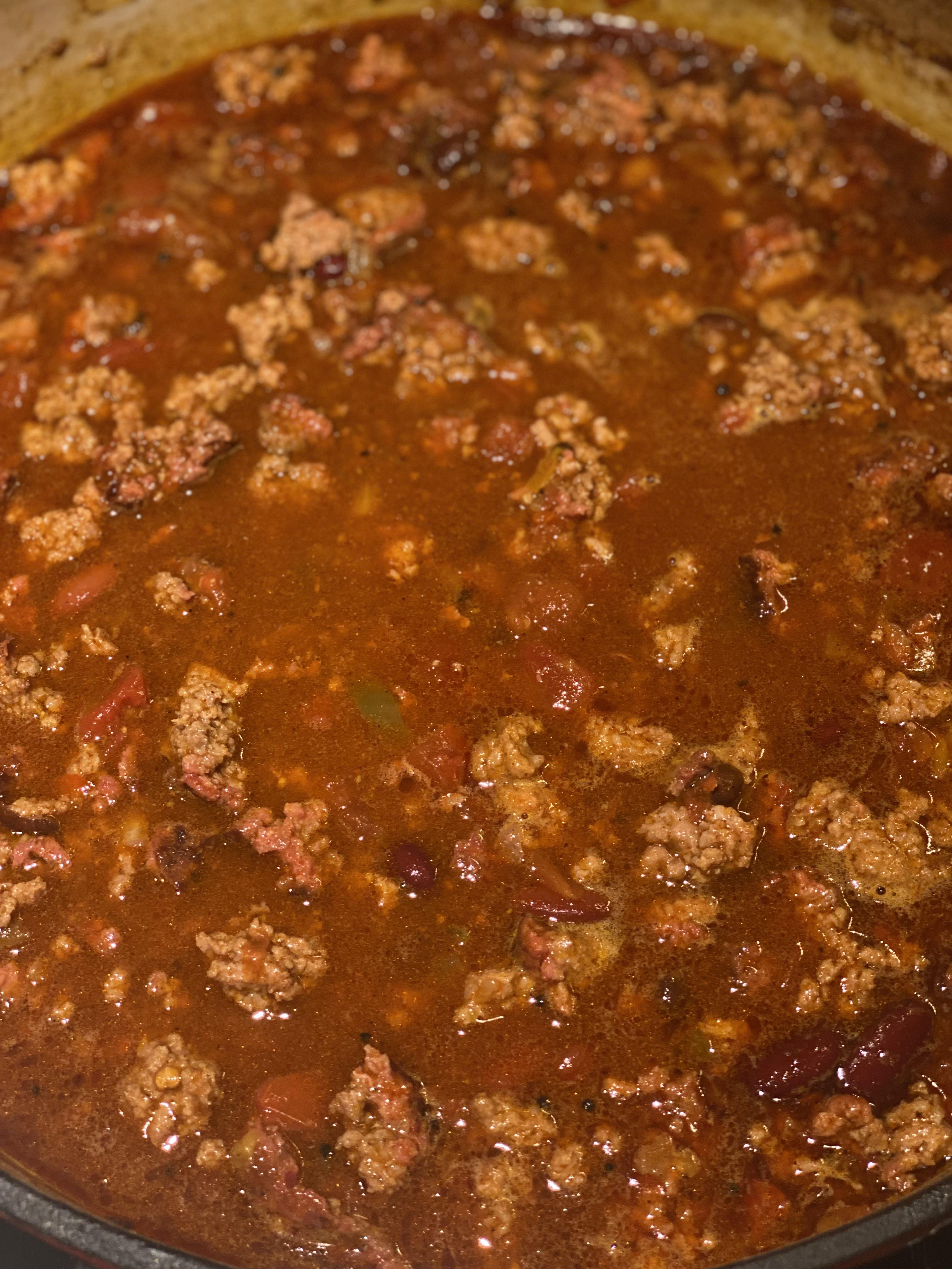 Over-the-top chili with bowls of stew, tortilla chips, and meatballs on a grill