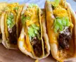 Homemade cheesy gordita crunch tacos with ground meat, lettuce, and melted cheese on a wooden surface