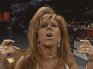 Terri Runnels with voluminous blonde hair and hoop earrings making a funny face and exhaling smoke