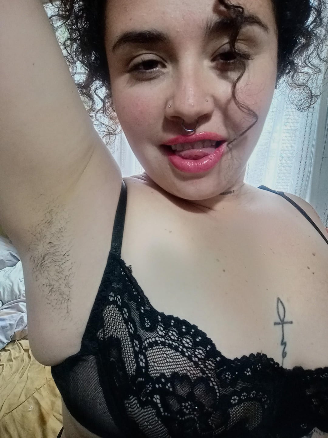Curvy latina with curly hair and a nose piercing in a black lace bra showing her hairy armpits