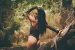 Curvy latina @hellkittyxxxo in a sparkly black bodysuit posing against a log in the forest