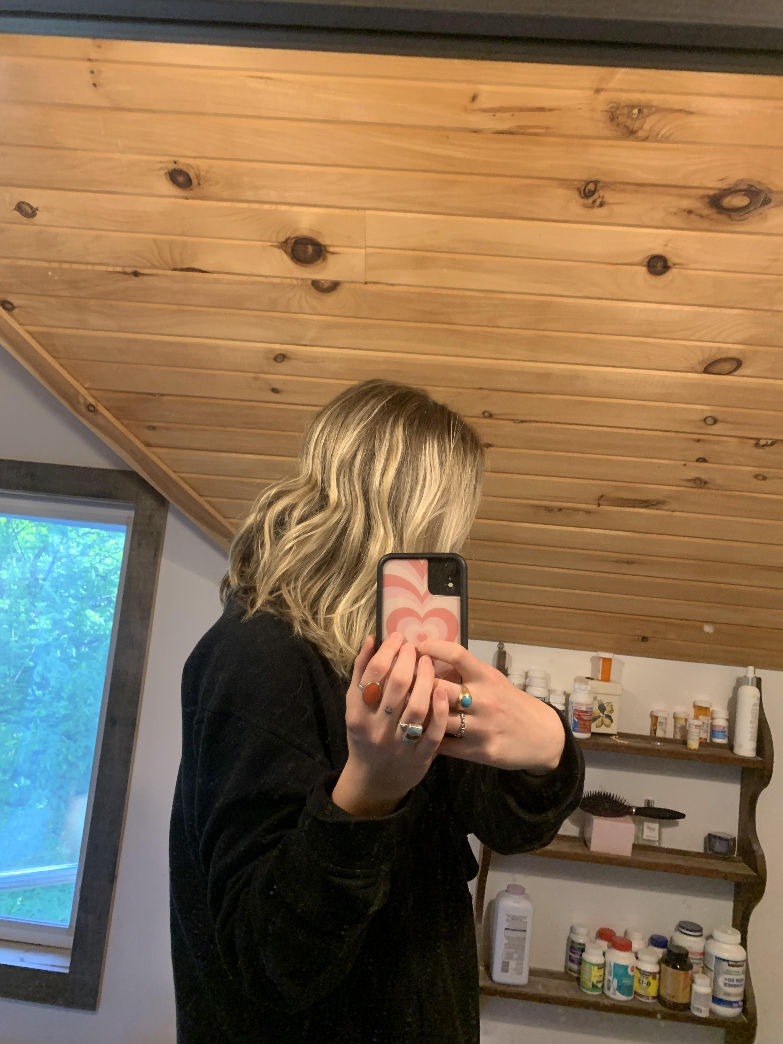 Blonde woman in a black hoodie taking mirror selfies to show her box dye blonde hair