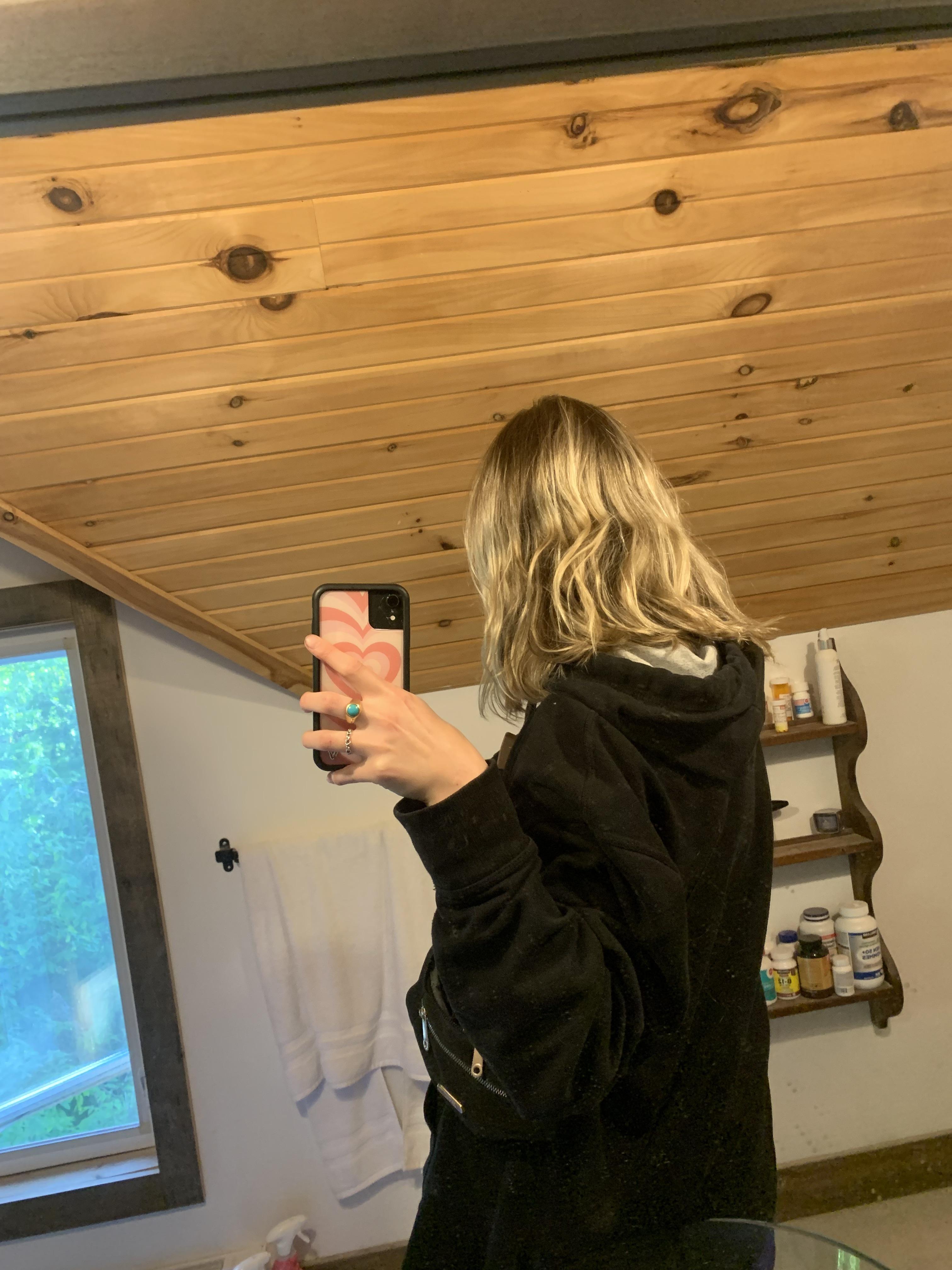 Blonde woman in a black hoodie taking mirror selfies to show her box dye blonde hair