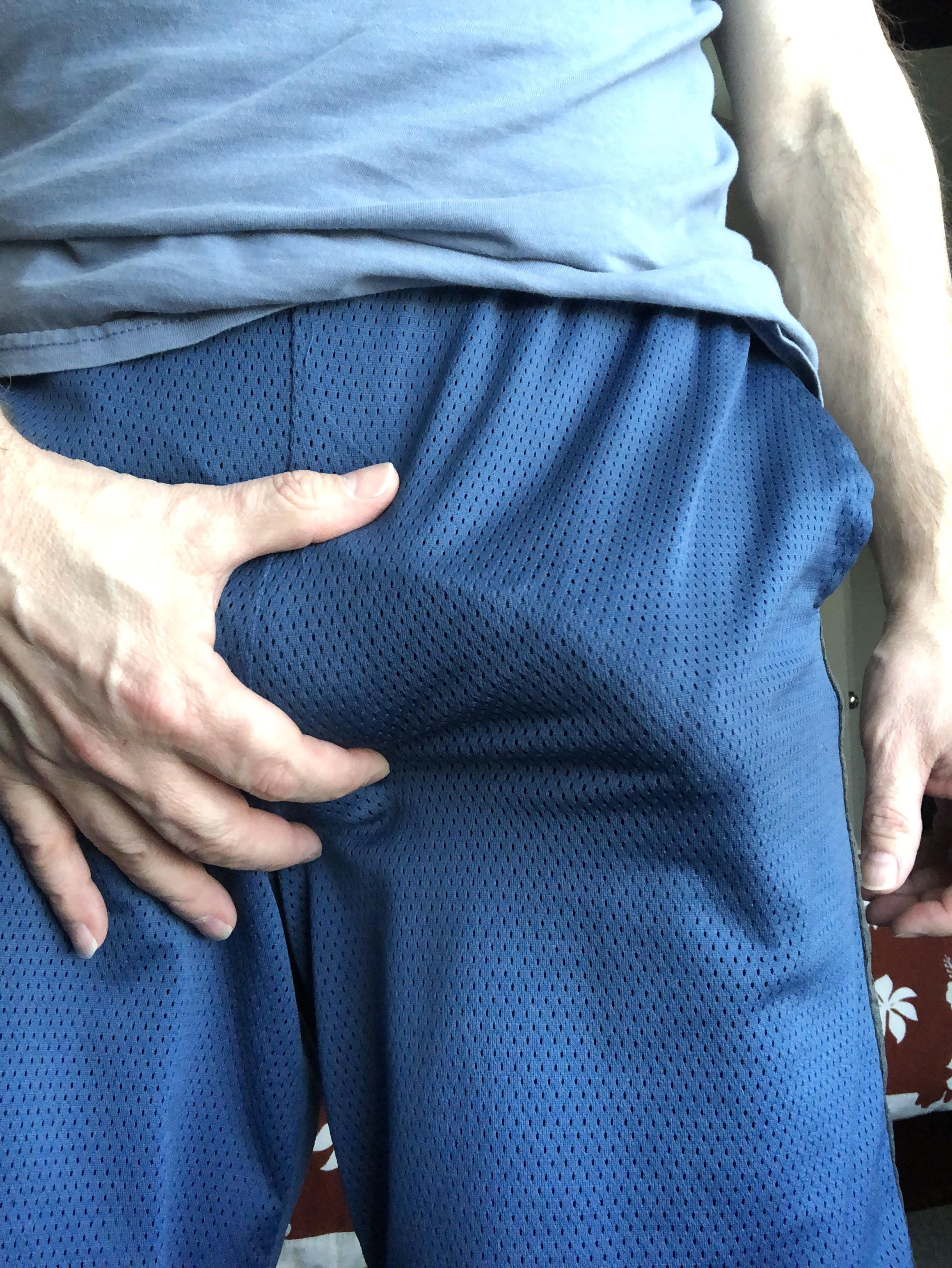 Athletic white man in red underwear and blue shorts posing for a selfie, touching his bulge