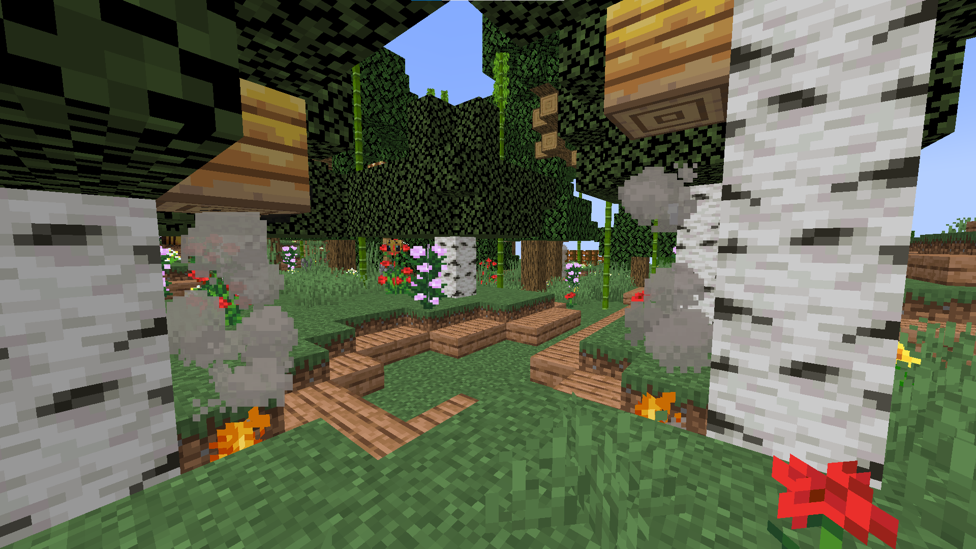 Minecraft survival builds featuring a base with flags, paths, and foliage in a beautiful landscape.