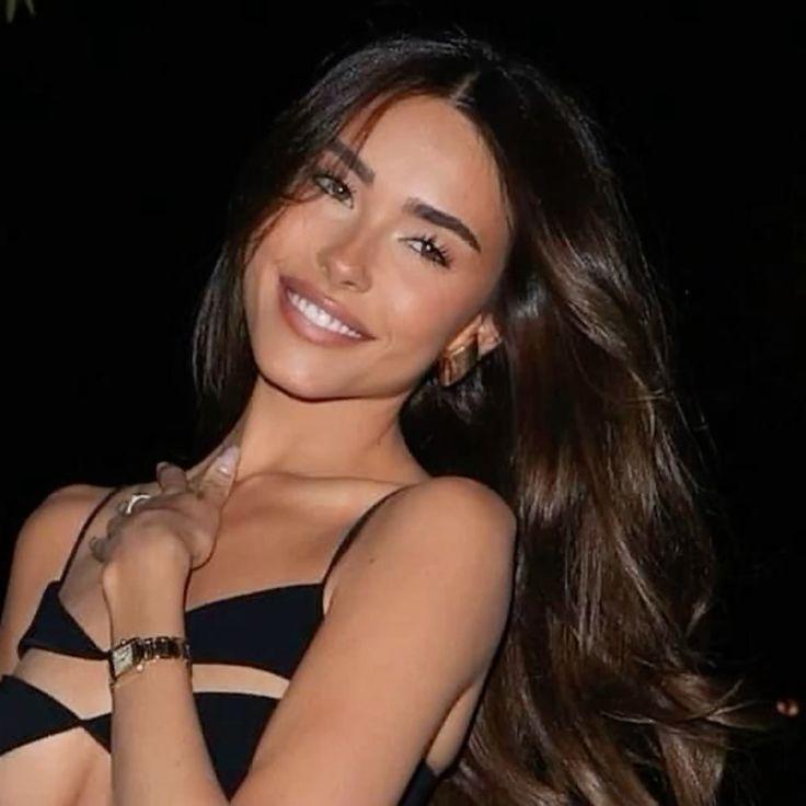 Madison Beer with long brown hair and tanned skin wearing a white dress, black clothing, and a blue wool sweater