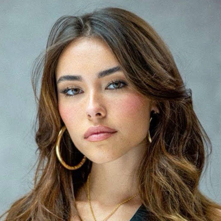 Madison Beer with long brown hair and tanned skin wearing a white dress, black clothing, and a blue wool sweater