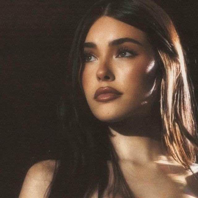 Madison Beer with long brown hair and tanned skin wearing a white dress, black clothing, and a blue wool sweater