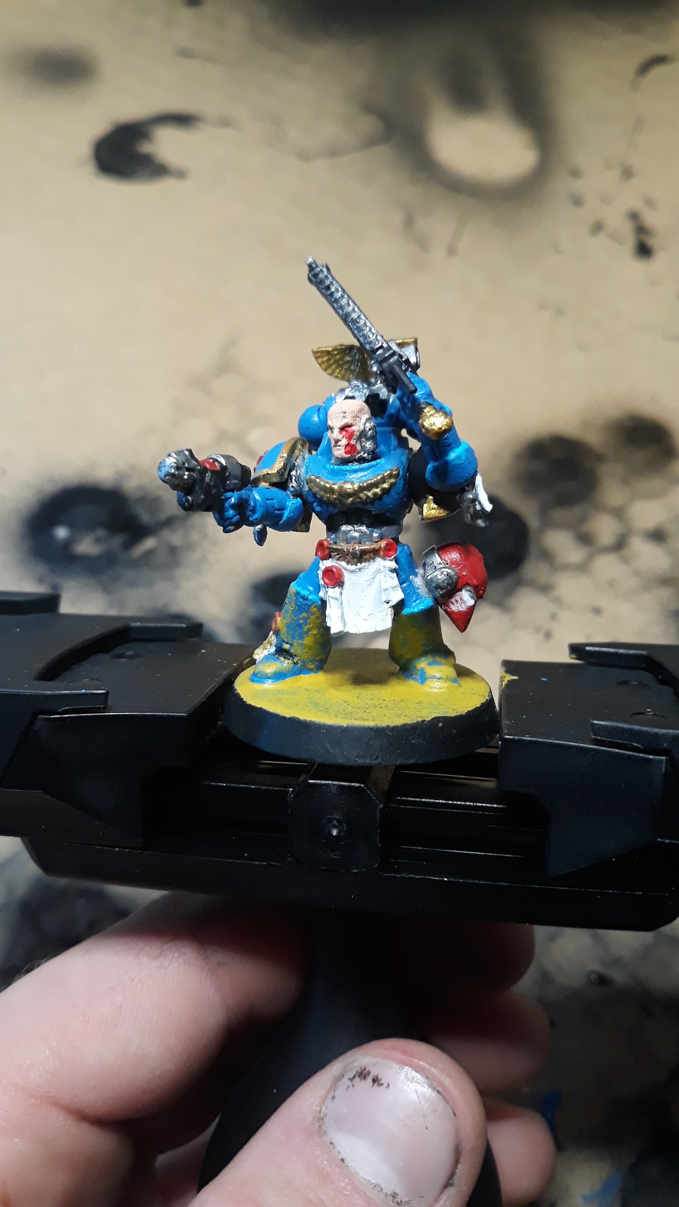 A hand holding a painted Warhammer miniature figurine of a blue armored warrior with a sword.
