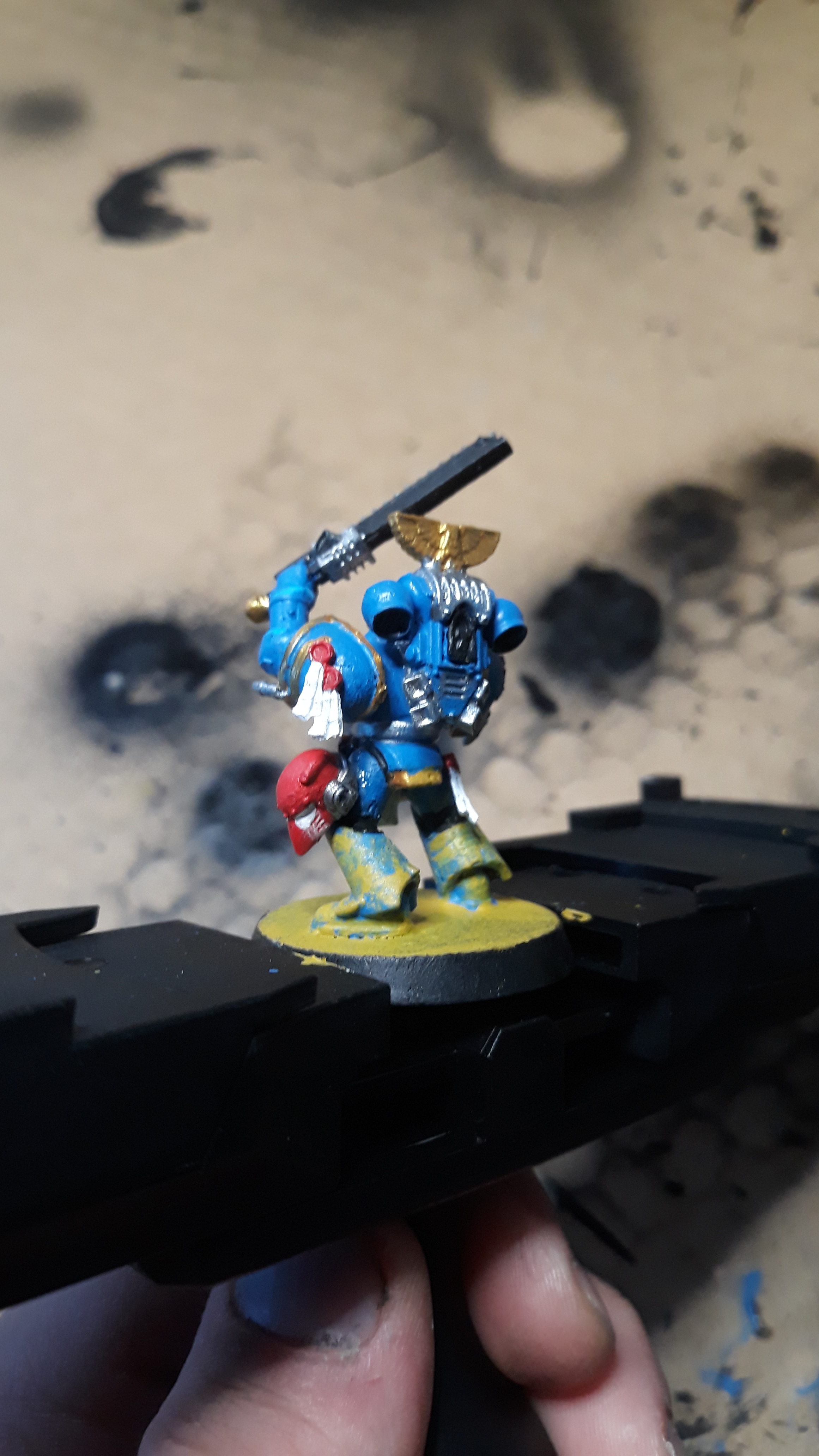 A hand holding a painted Warhammer miniature figurine of a blue armored warrior with a sword.