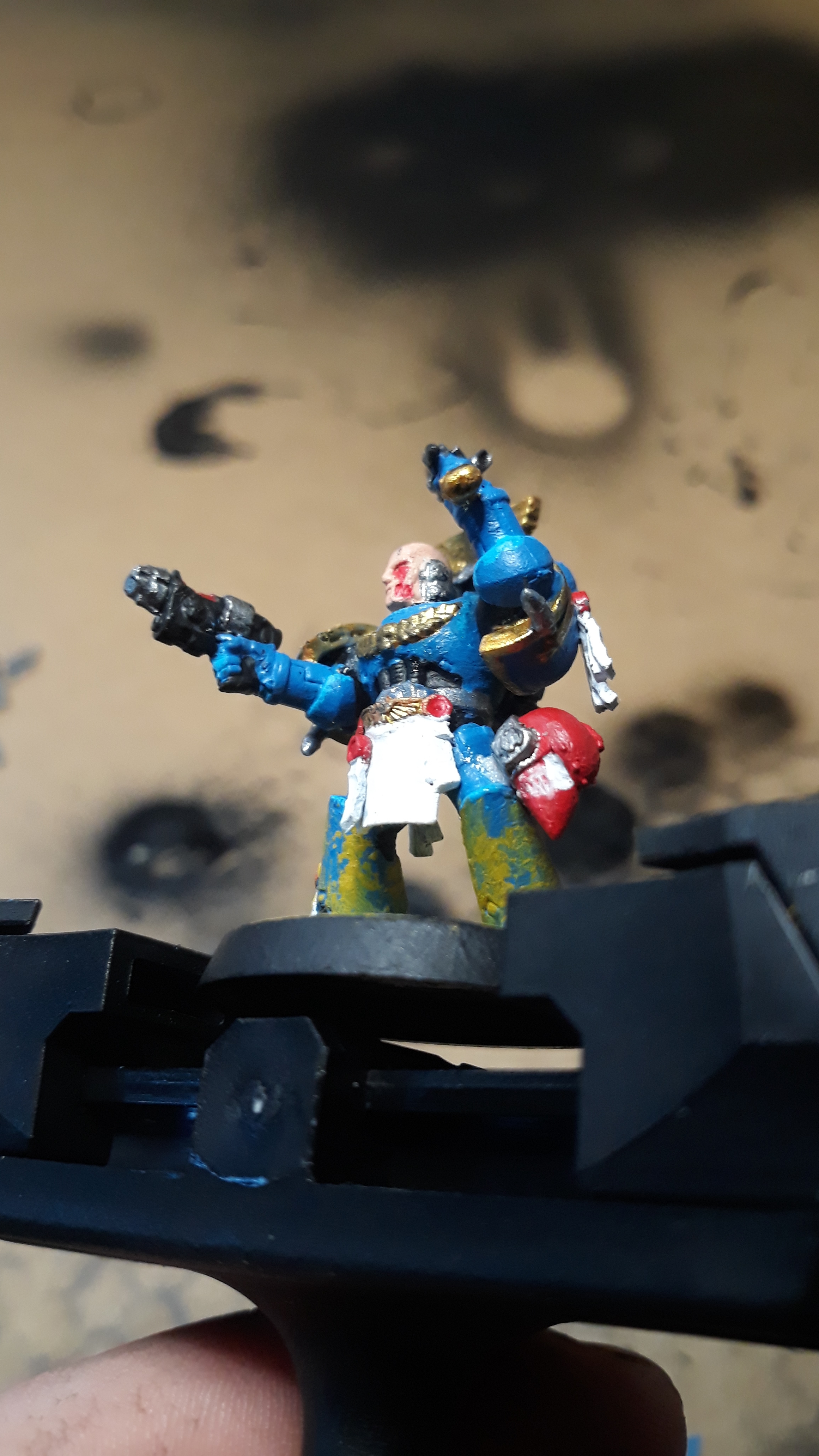 A hand holding a painted Warhammer miniature figurine of a blue armored warrior with a sword.
