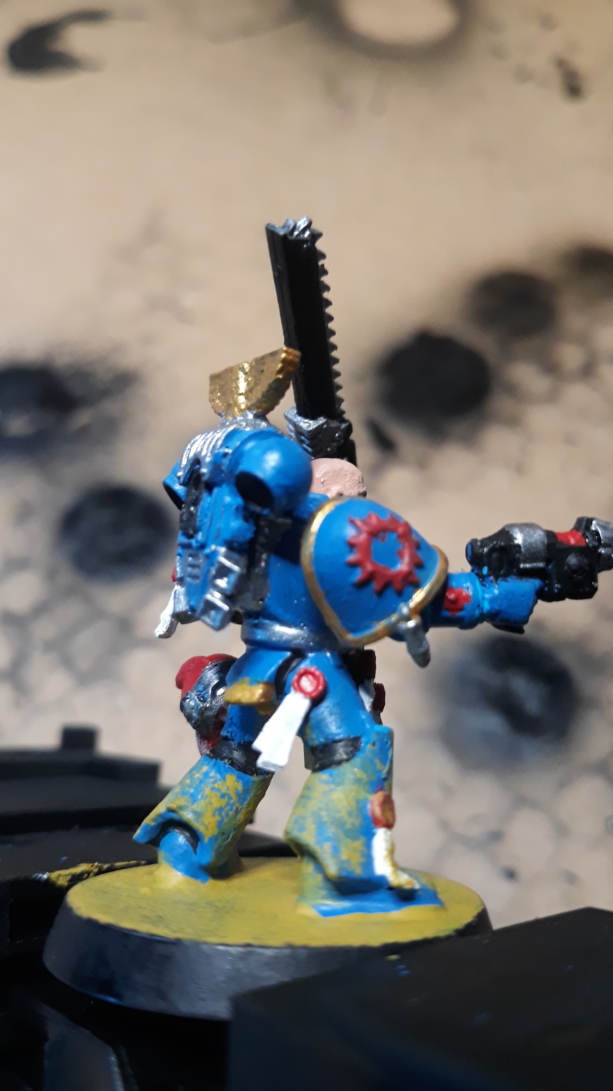 A hand holding a painted Warhammer miniature figurine of a blue armored warrior with a sword.