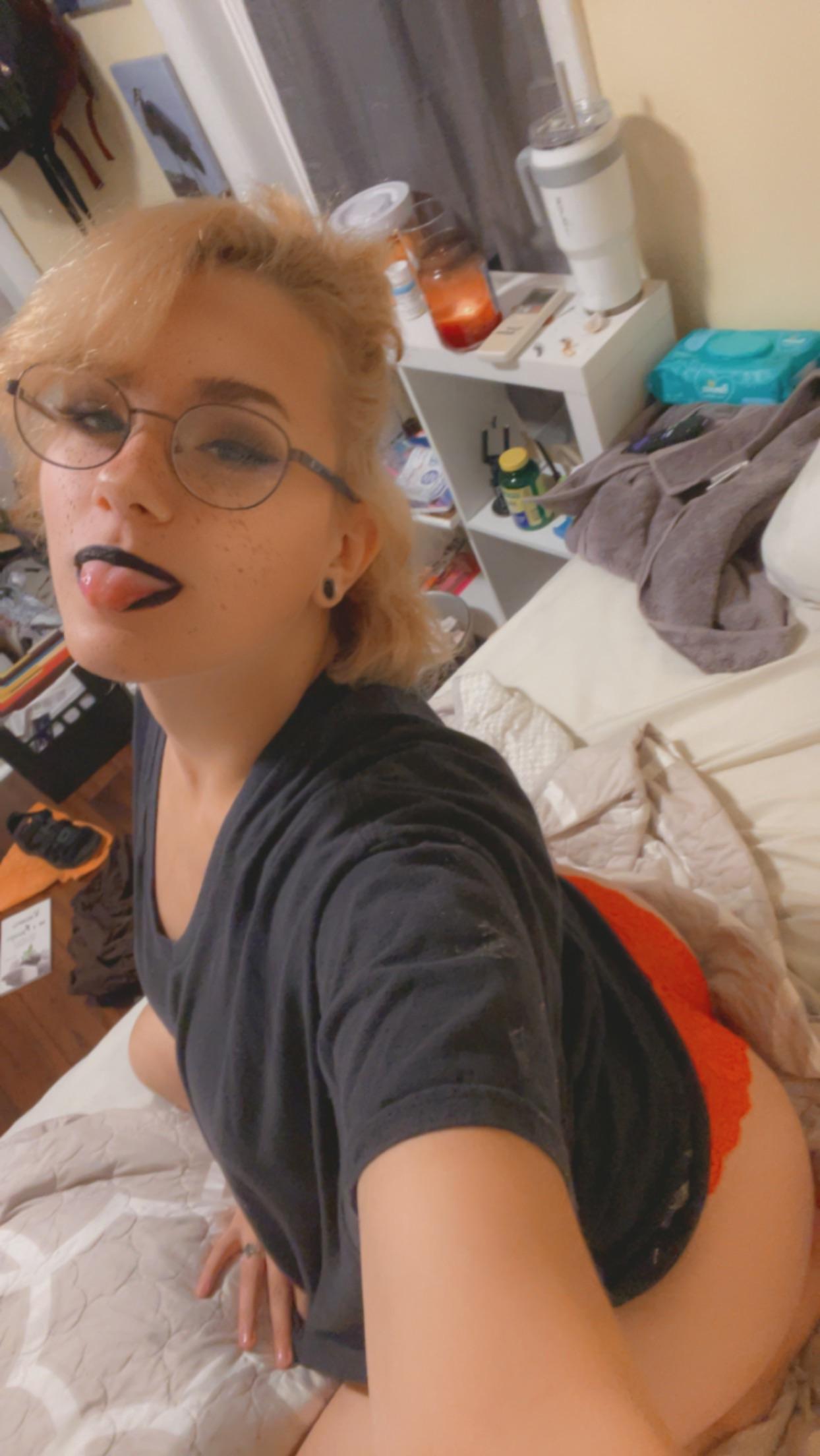 Pregnant blonde woman in a black t-shirt and panties posing with a belly bulge