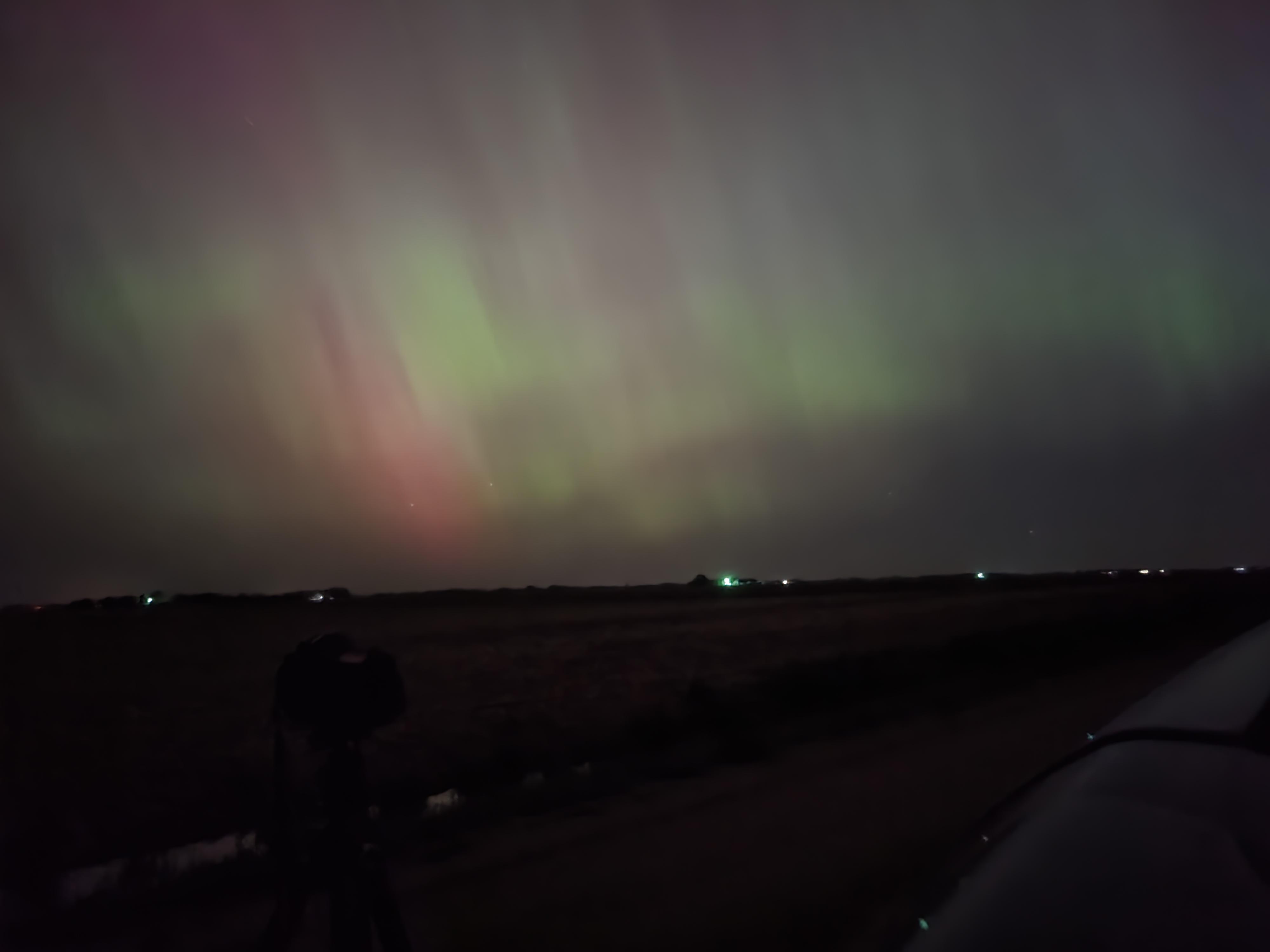Camera on a tripod silhouetted against purple and green aurora borealis in Nebraska