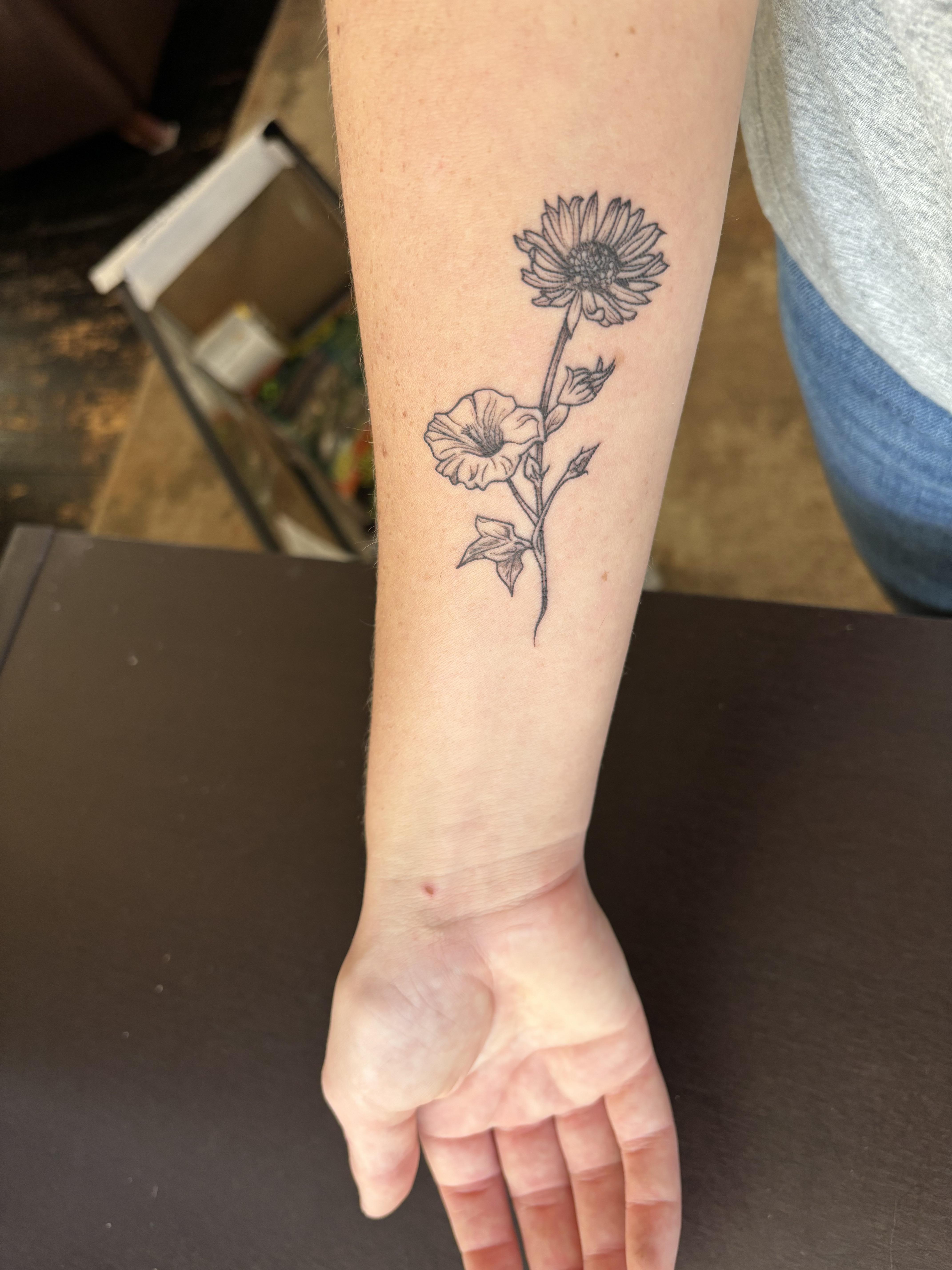 Fine line black ink floral tattoo of two flowers on a fair-skinned person's forearm