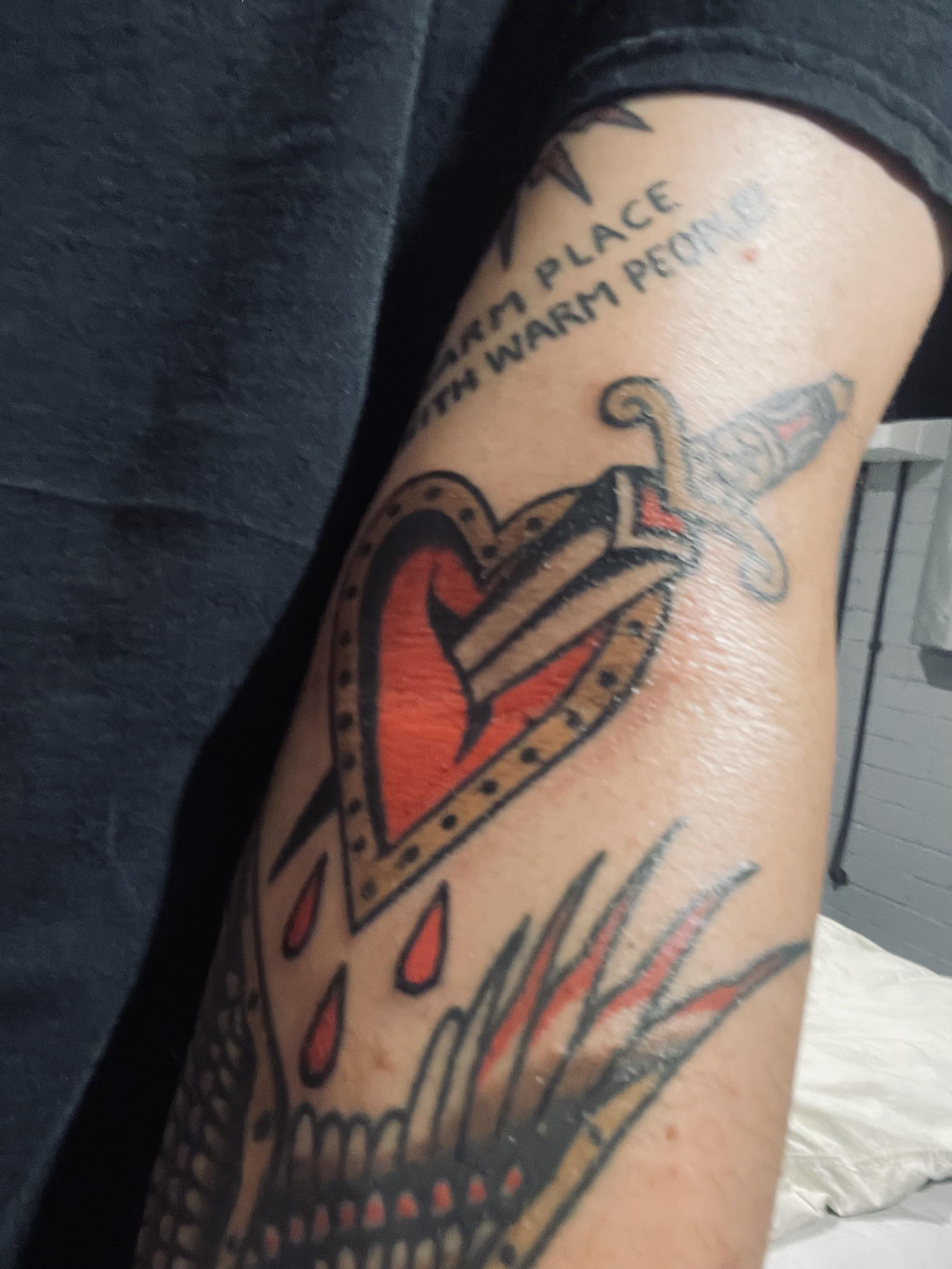 Traditional tattoos of a heart with a sword and a dragon on a person's arm with pale skin