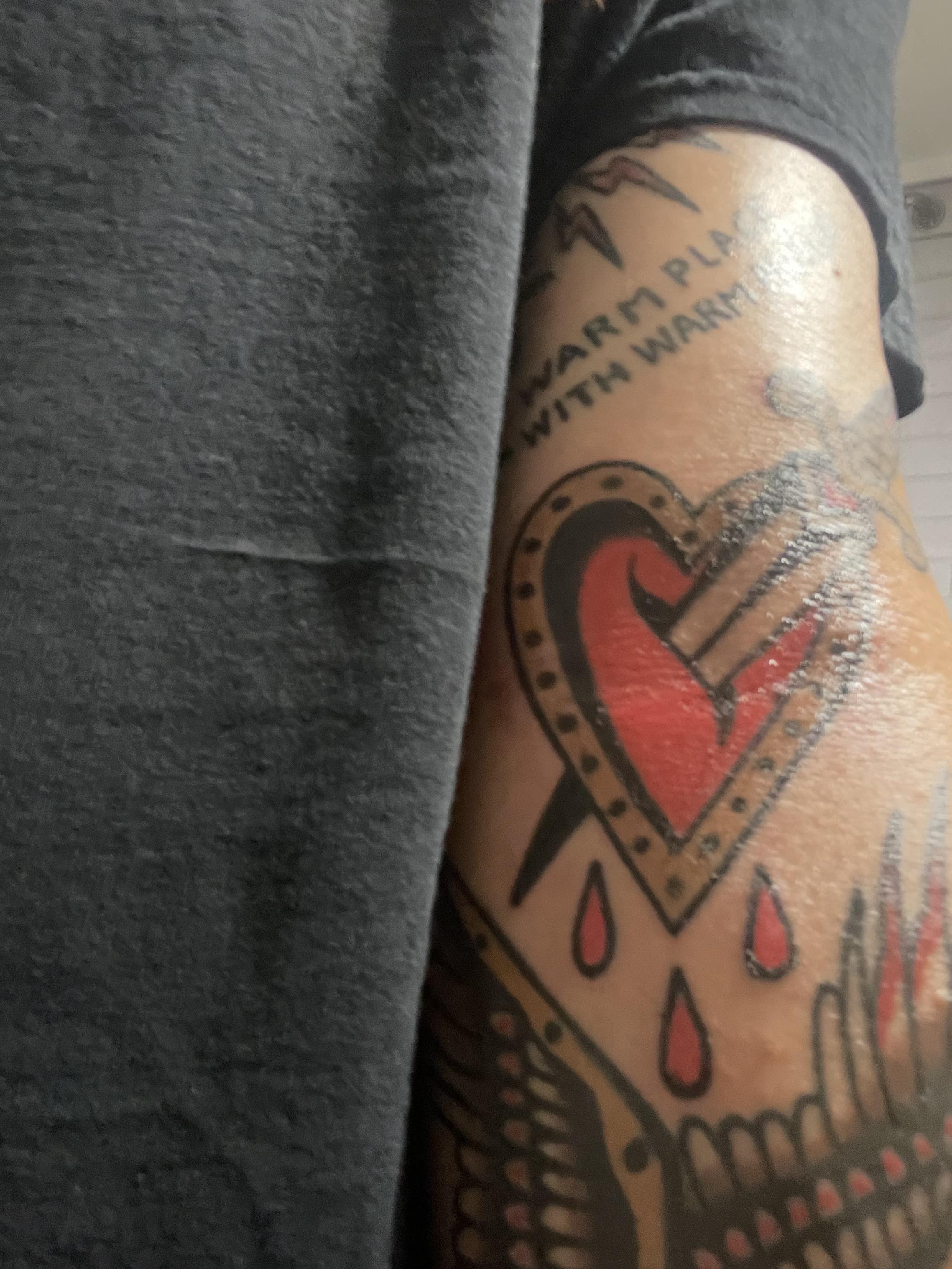 Traditional tattoos of a heart with a sword and a dragon on a person's arm with pale skin