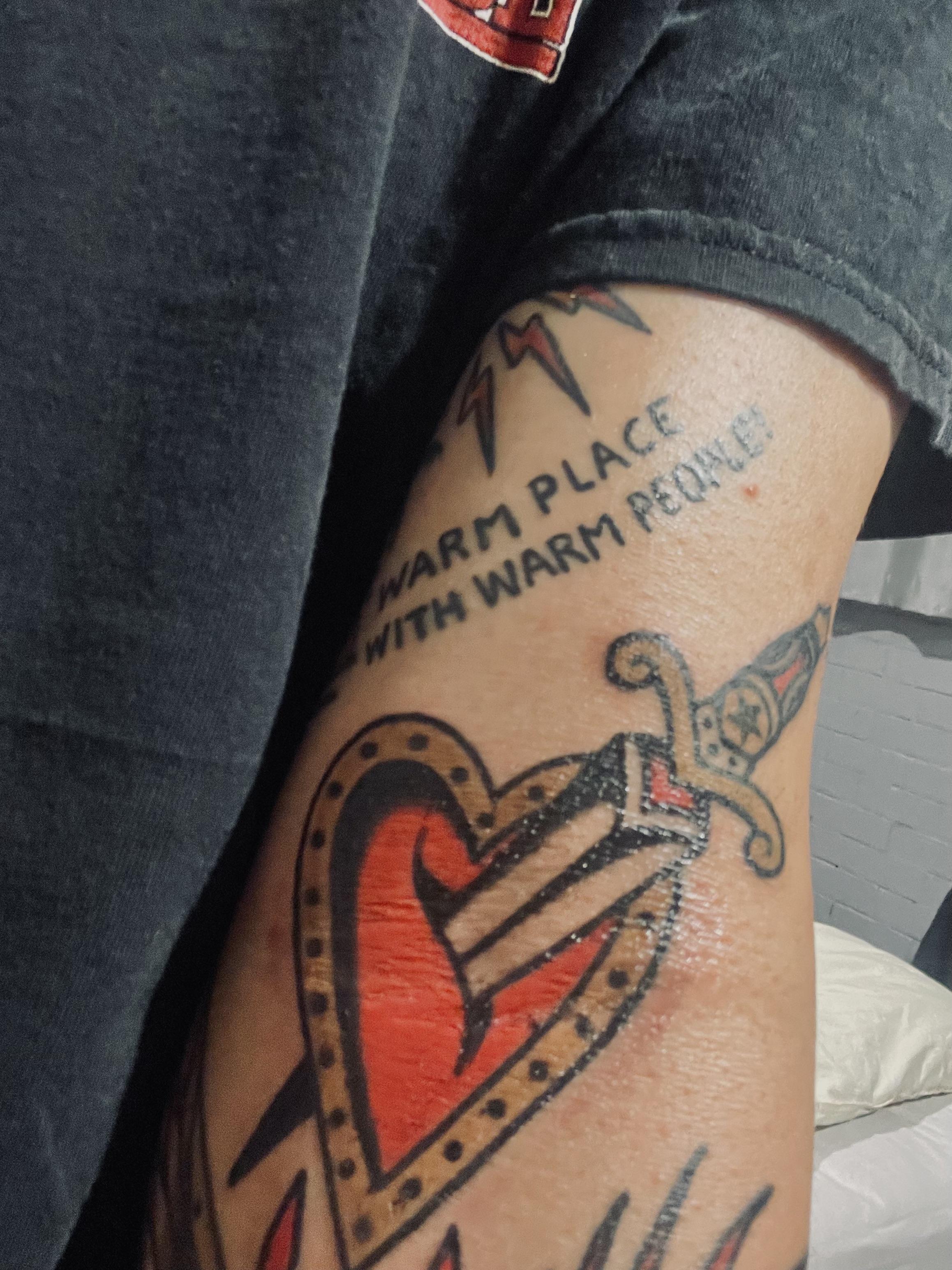 Traditional tattoos of a heart with a sword and a dragon on a person's arm with pale skin