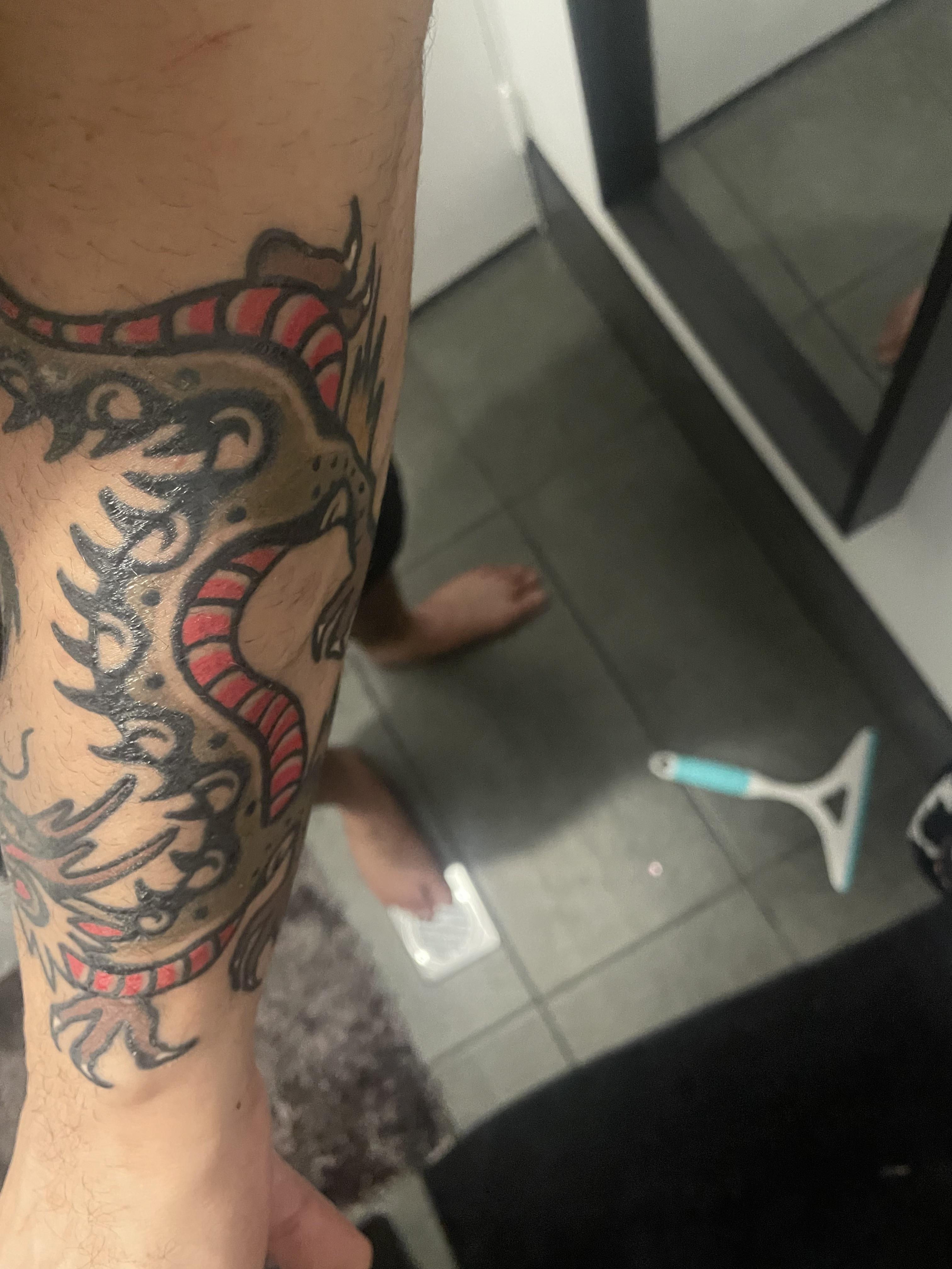 Traditional tattoos of a heart with a sword and a dragon on a person's arm with pale skin