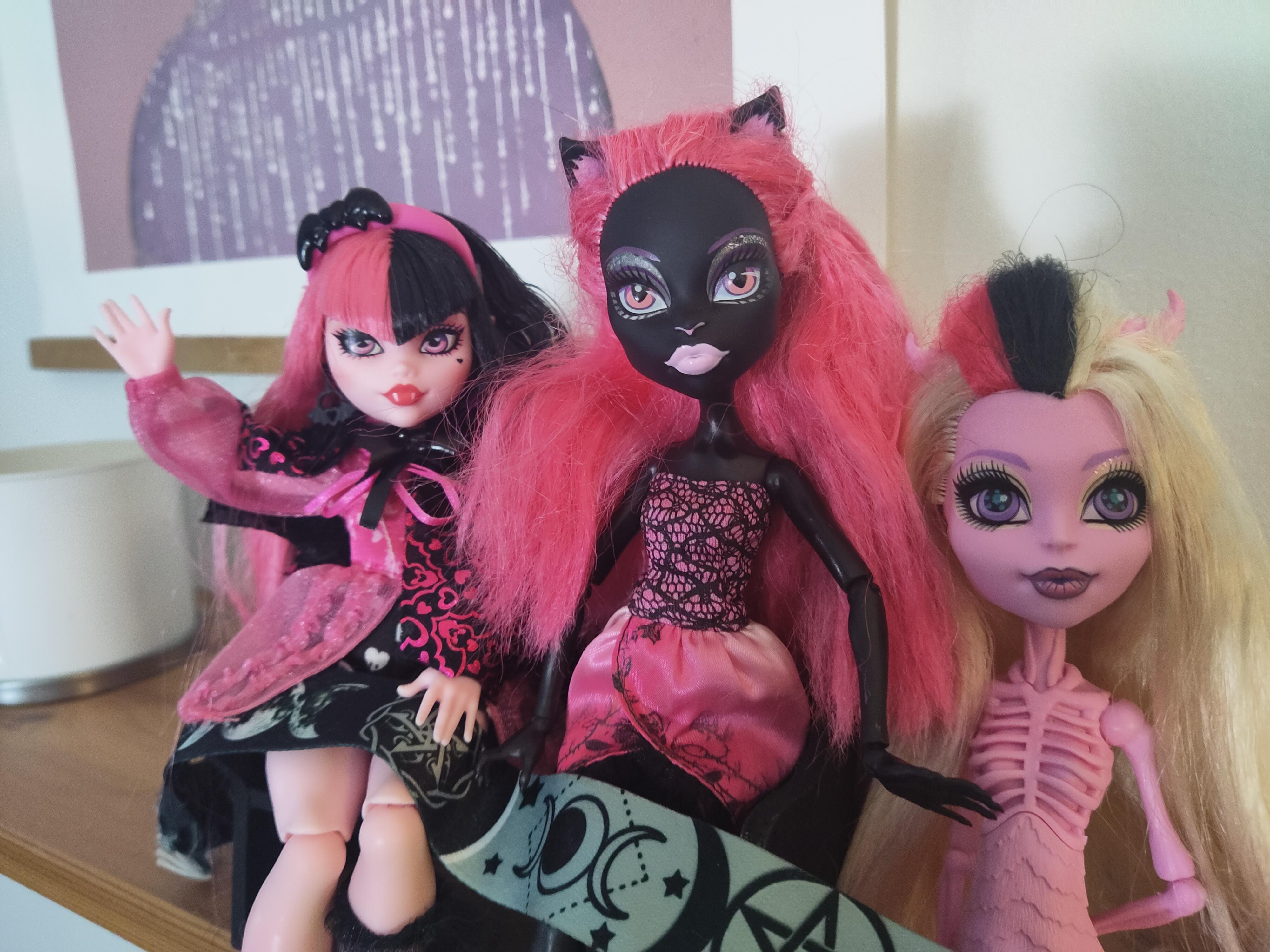 Three Monster High dolls with pink and blonde hair wearing black and pink lace and satin dresses on a shelf