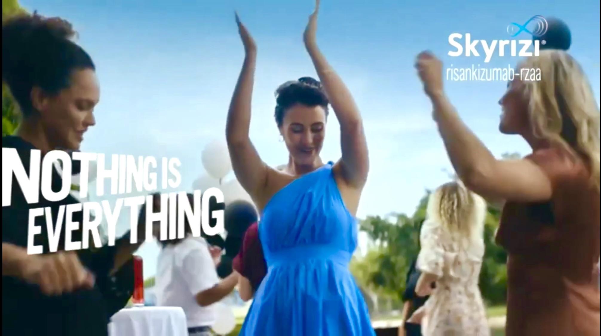 Group of beautiful women in floral, blue, white, and black summer dresses dancing outdoors under a blue sky