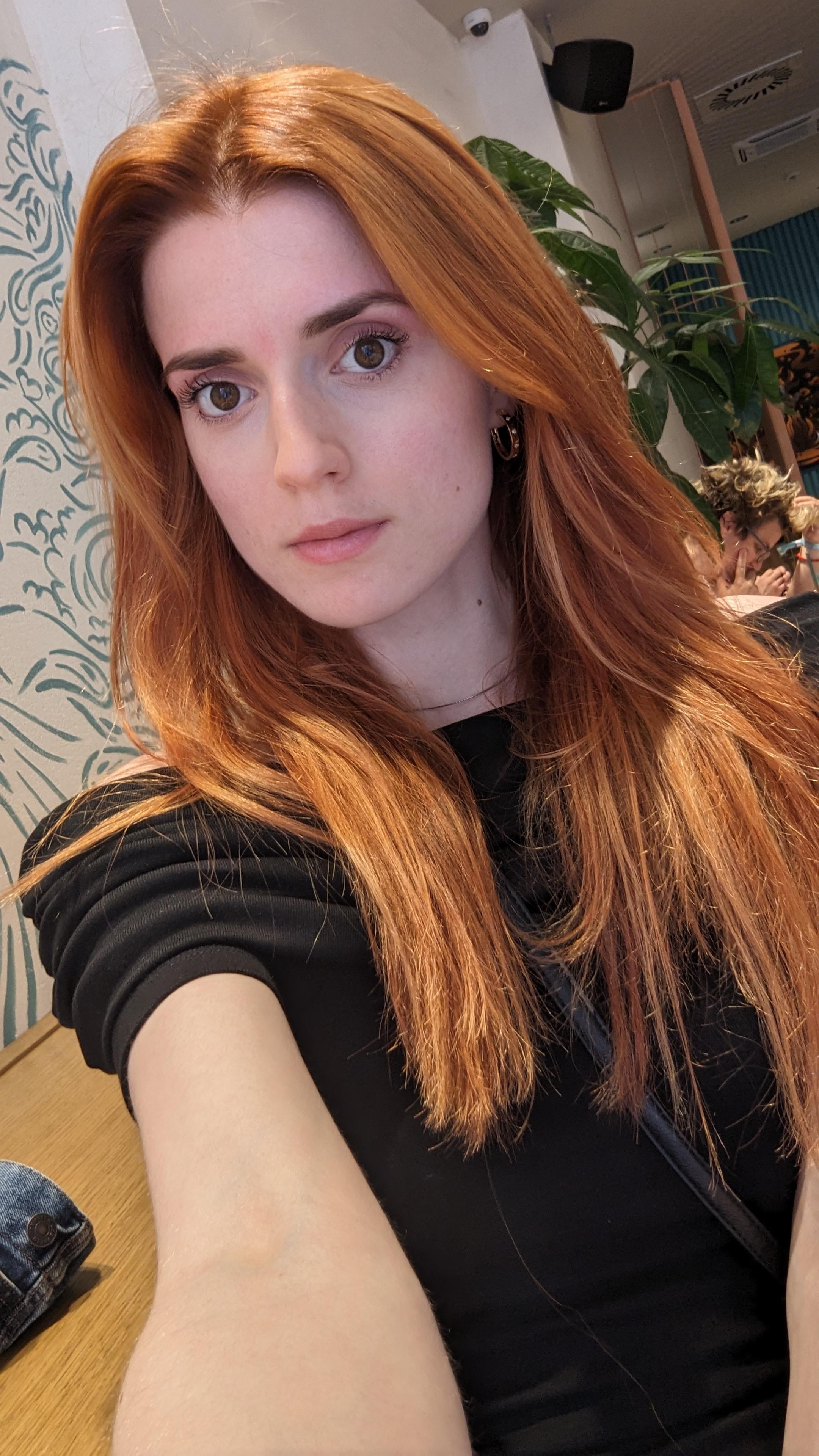 A slender woman with long red hair and pale skin wearing a black t-shirt, blue tank top, and black midi dress.