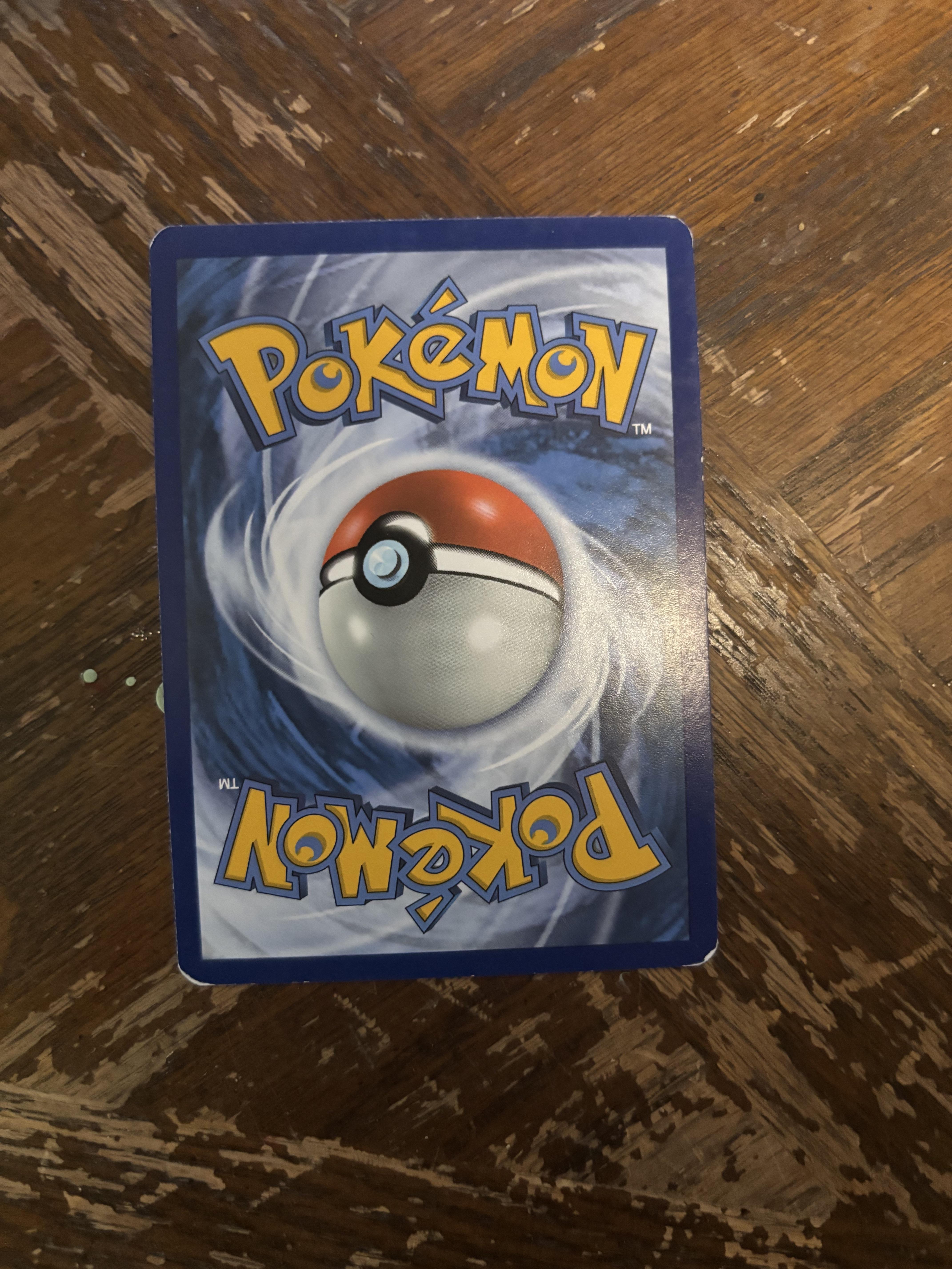 Front and back views of a cursed Pokemon card featuring Gyarados on a wooden surface.